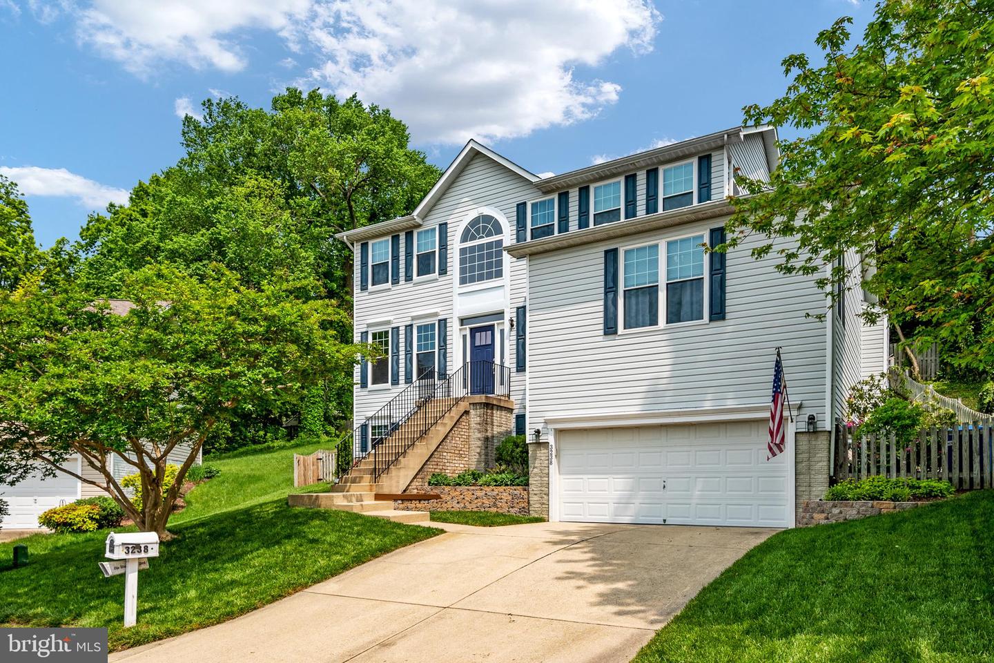 Two-story gray house with blue shutters, brick entry steps, double garage, and landscaped front lawn.
