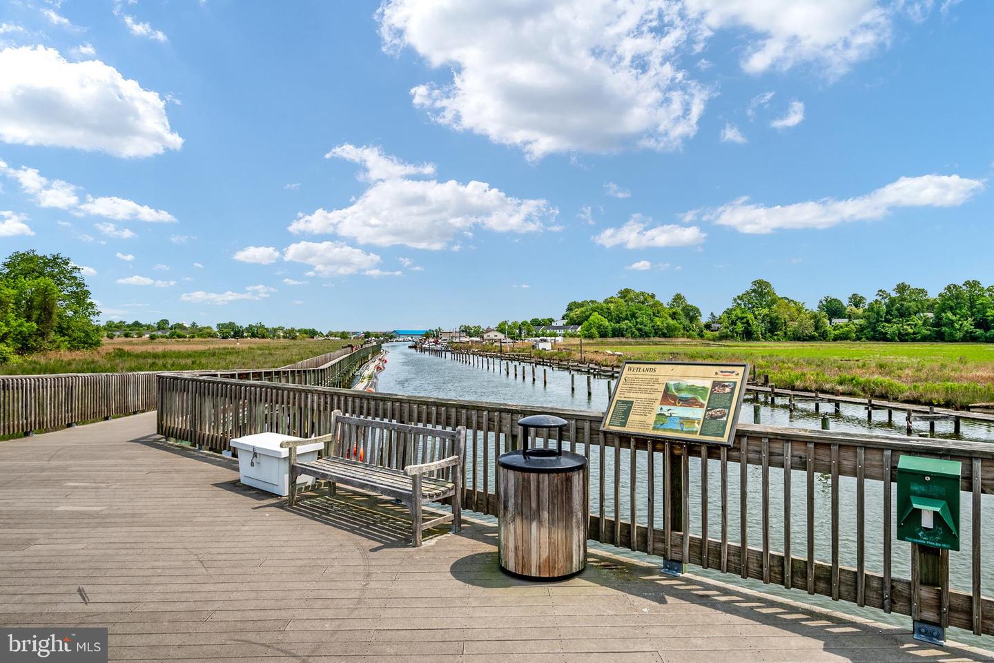 Waterfront boardwalk beside a channel, with marsh grasses and a wetlands sign.