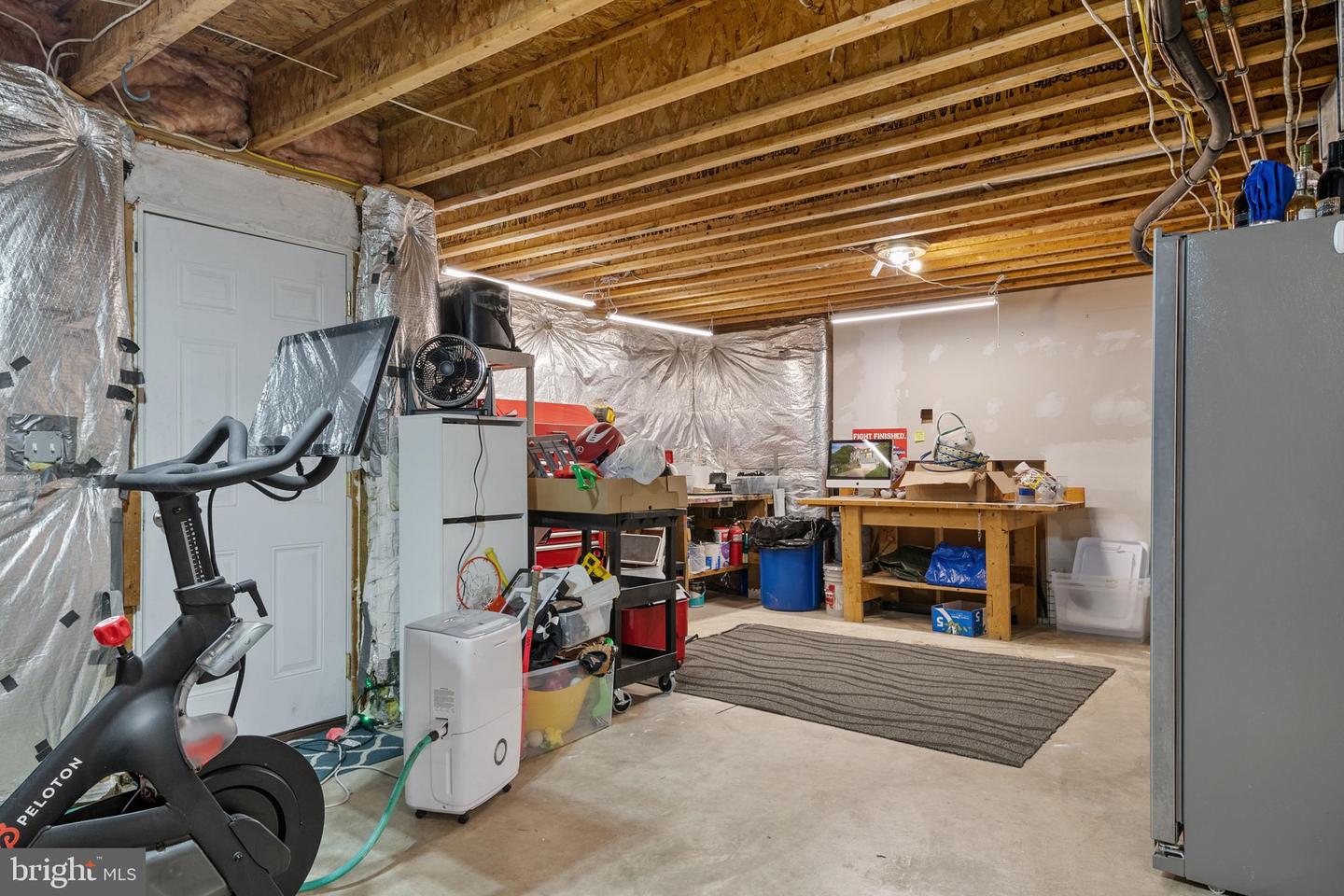 Unfinished basement with exposed joists, a Peloton bike, and a workbench.