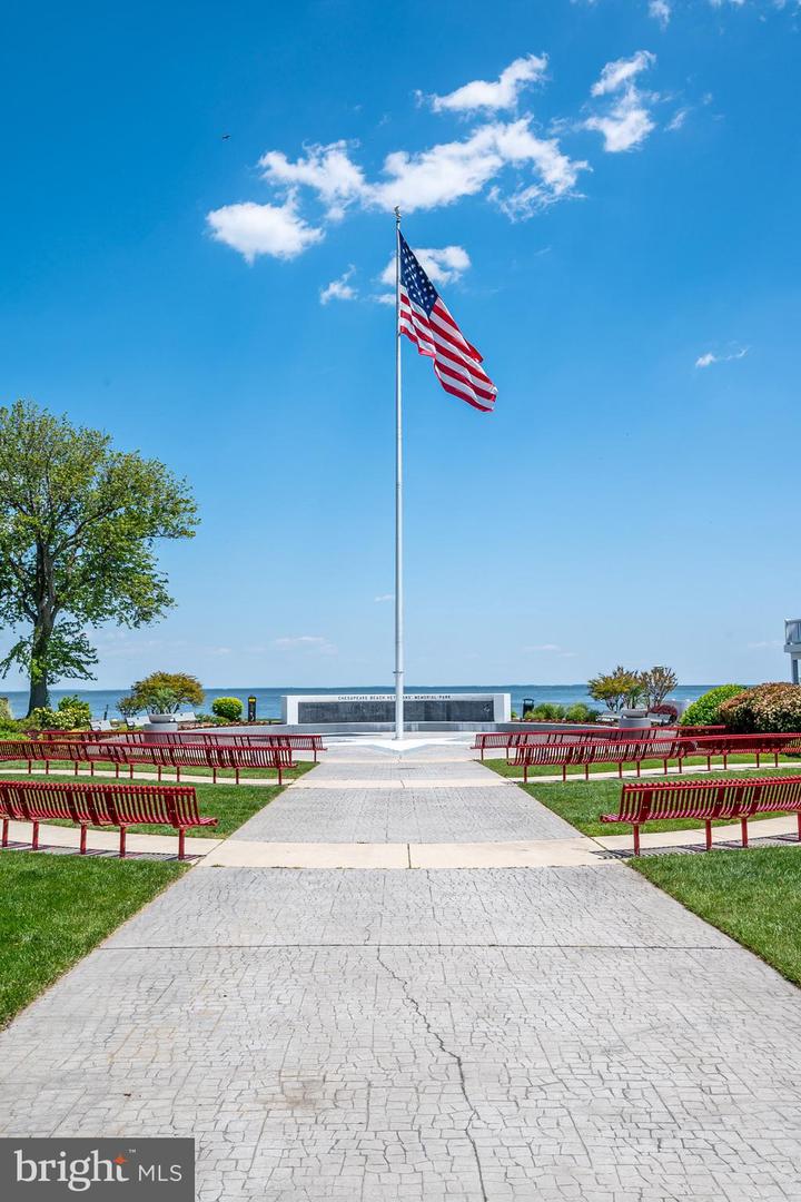 Waterfront memorial park with an American flag, red benches, and a paved walkway leading to the water.