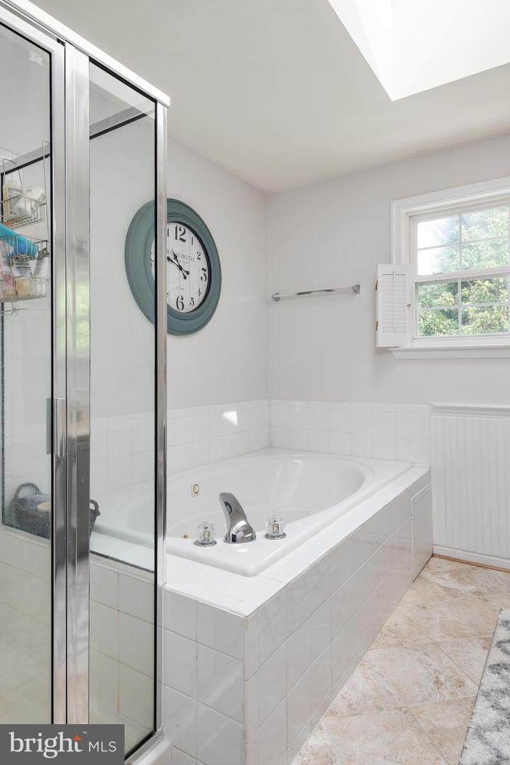 Bathroom with a built-in jetted tub, glass shower enclosure, and teal wall clock.