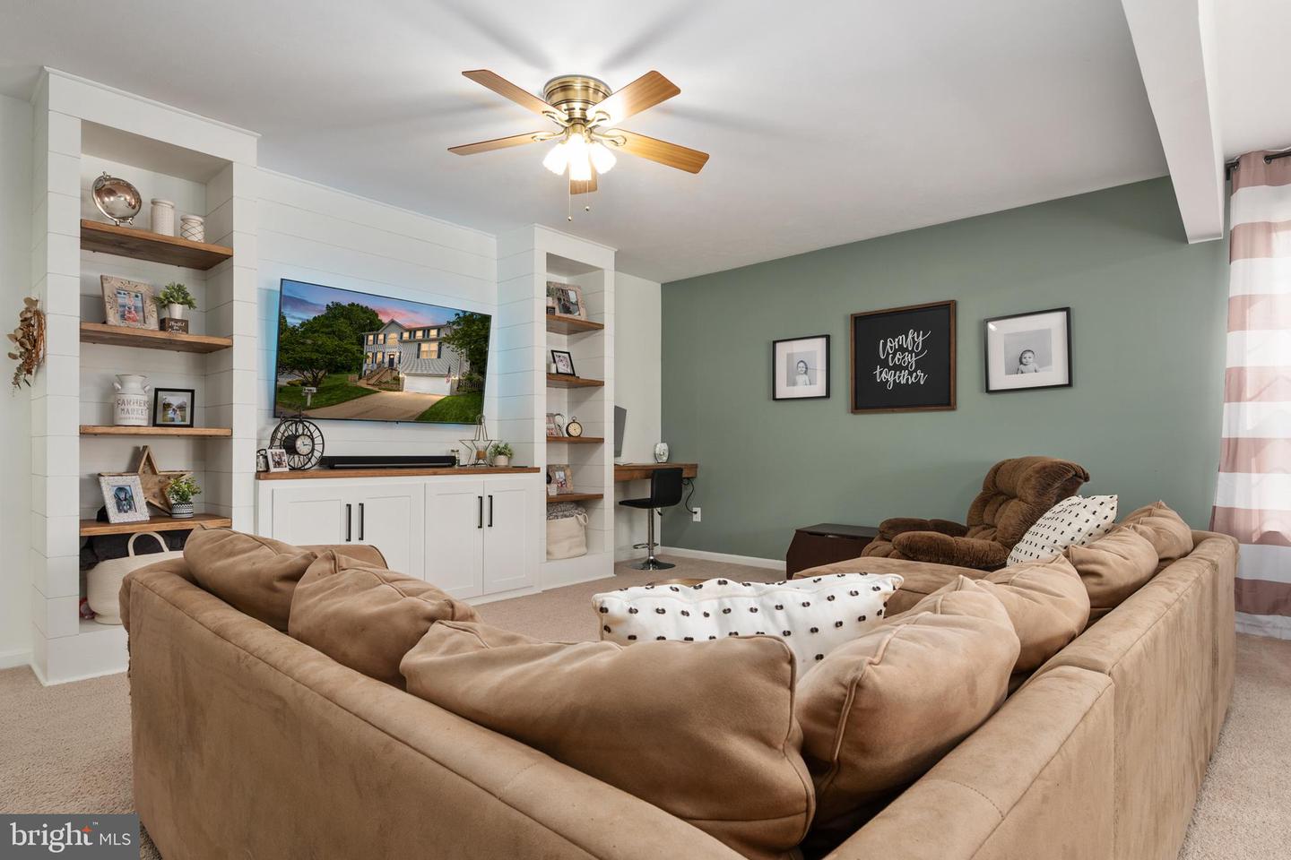 Furnished living room with a tan sectional, built-in media shelving, and a green accent wall.