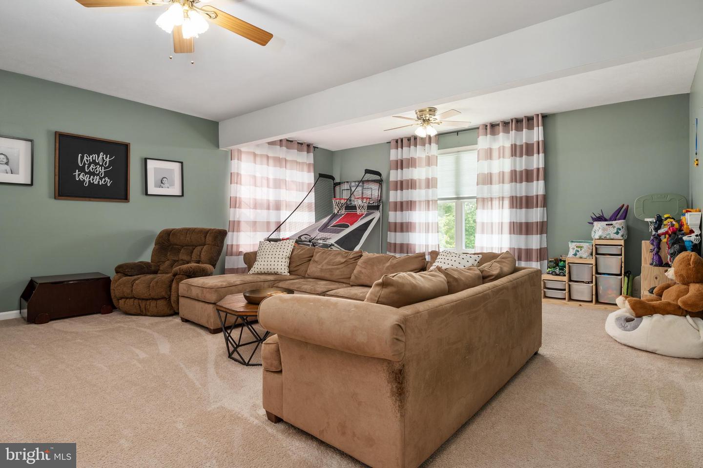 Basement recreation room with a sectional sofa, basketball arcade game, and children’s play area.