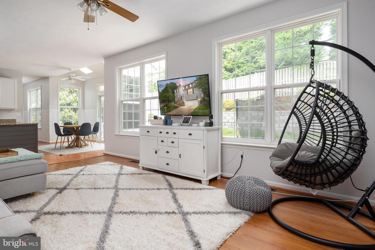 Bright living room with large windows, hardwood floors, a white rug, and a hanging egg chair.