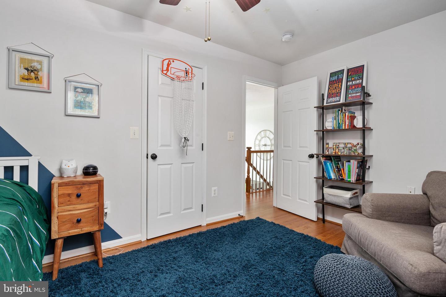 Bedroom with a miniature basketball hoop on the door, blue rug, green bed, and bookcase of books.