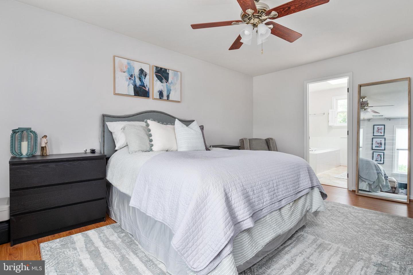 Primary bedroom with white bedding, abstract art, and a doorway to the bathroom.