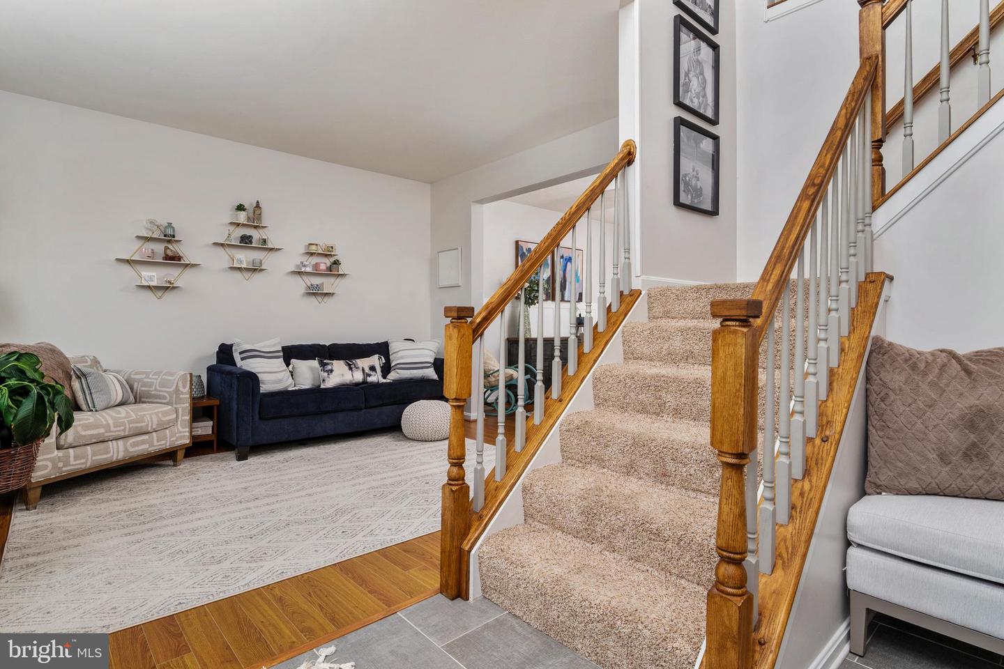 Furnished living room beside a carpeted staircase with warm wood railings and hardwood flooring.