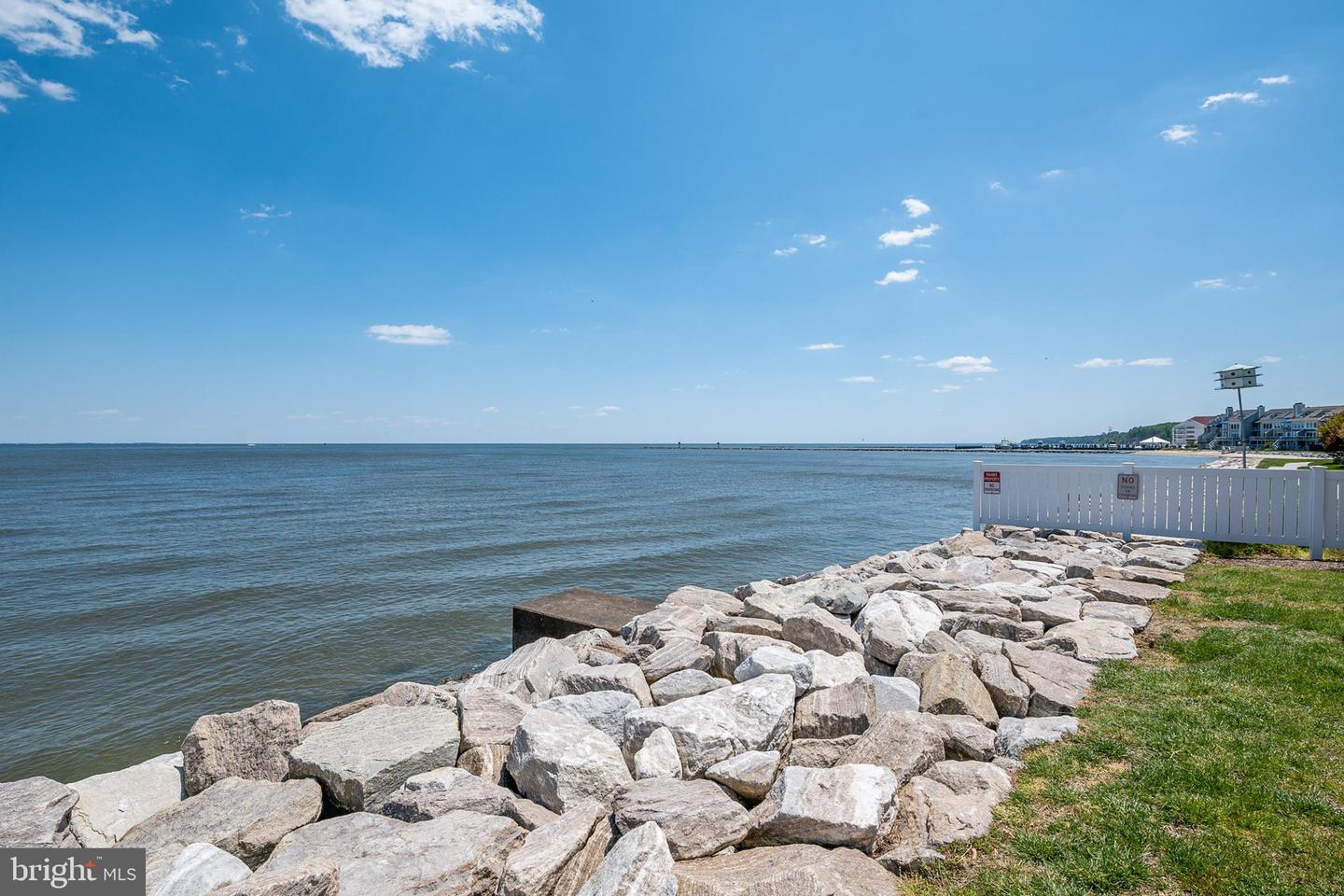 Chesapeake Bay shoreline with large rocks, a white fence, and homes along the distant shore.