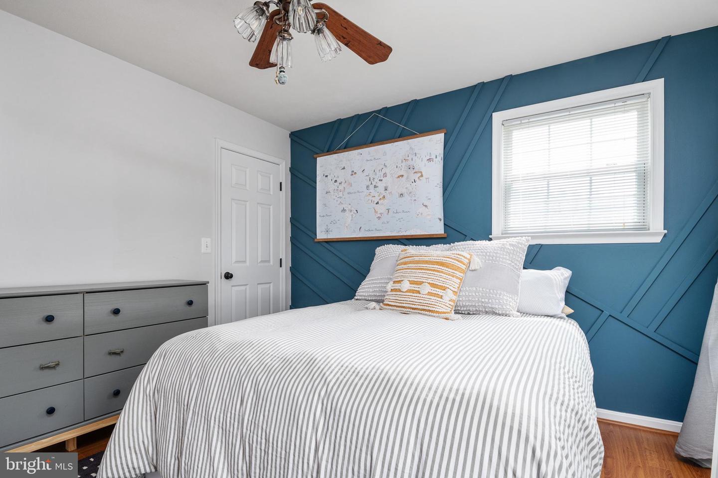 Bedroom with striped bedding, a teal geometric accent wall, and a gray dresser.