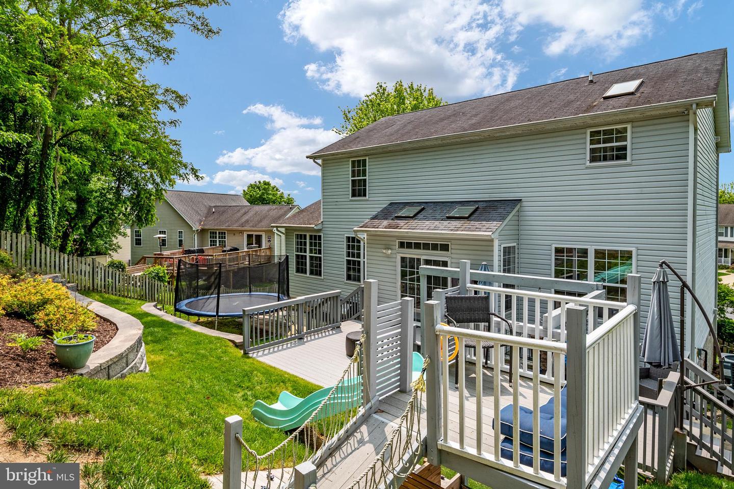 Home’s rear deck overlooks a fenced yard with a trampoline and children’s slide.