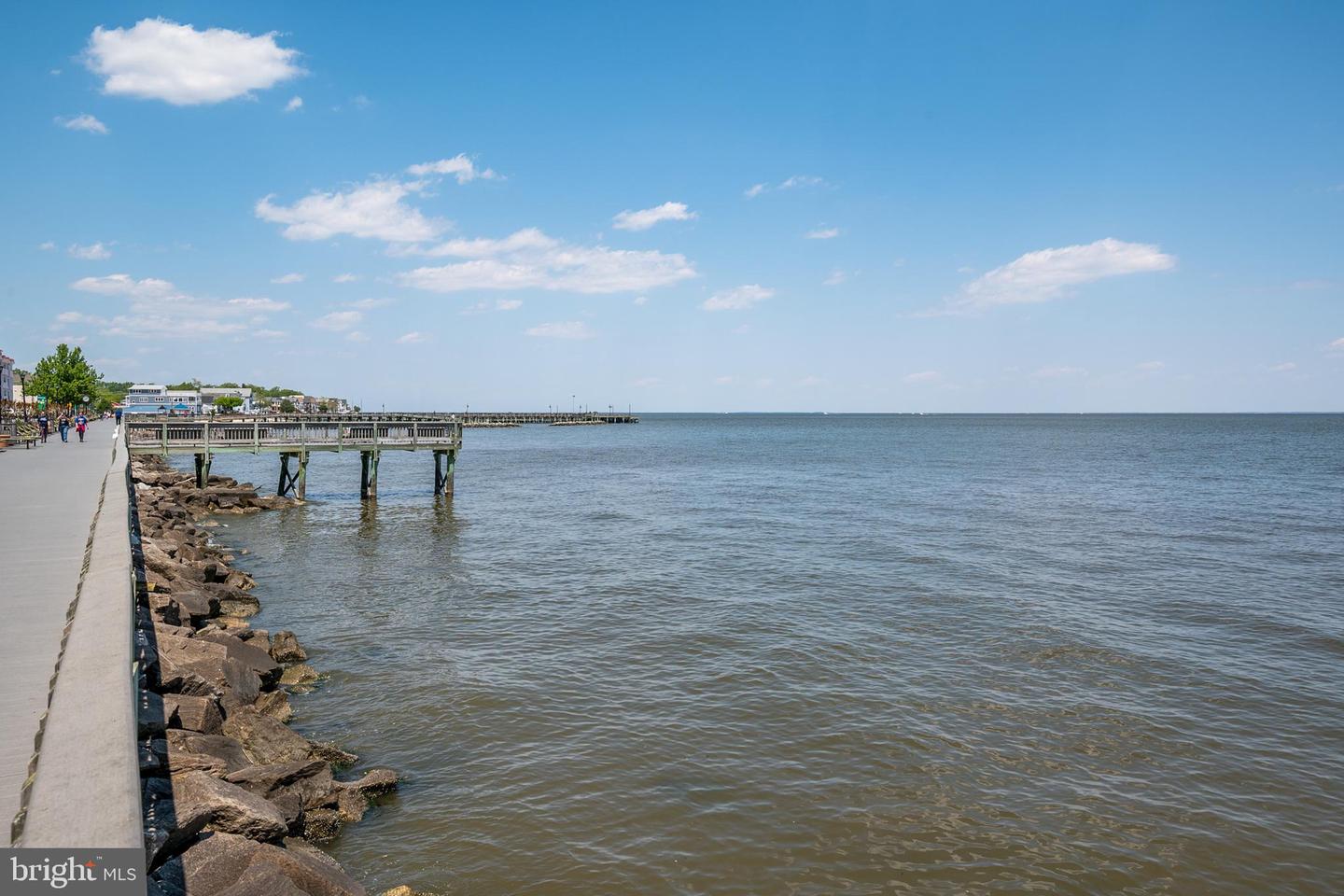 Waterfront promenade and wooden pier beside open water under a clear blue sky.