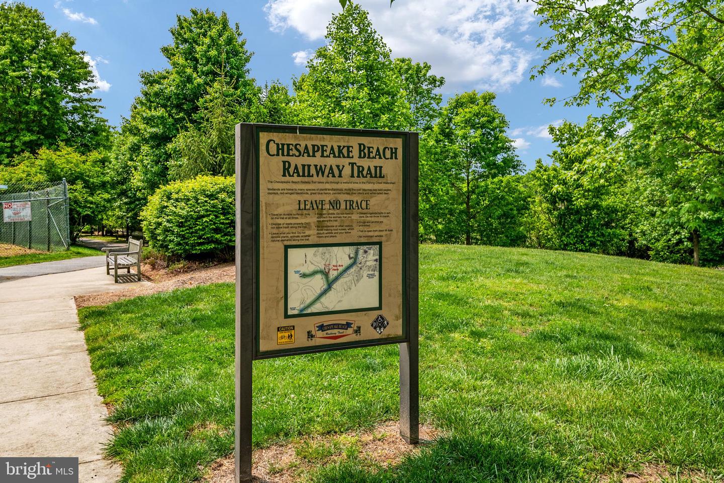 Chesapeake Beach Railway Trail sign beside a paved path, grassy lawn, and wooded park.