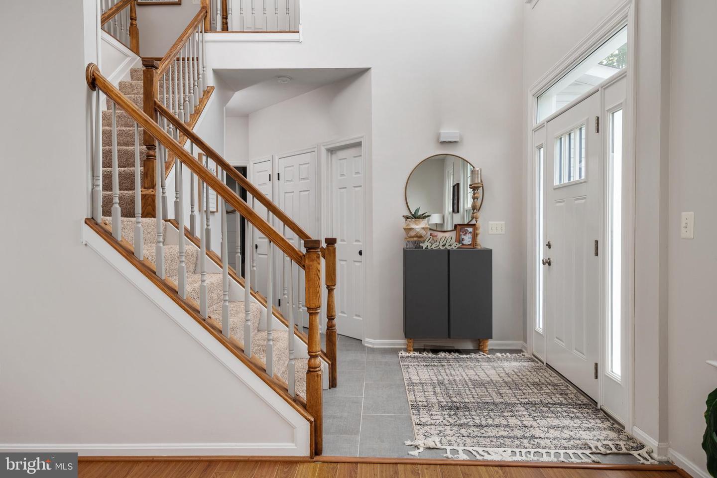 Entry foyer with a carpeted staircase, wood railings, patterned rug, and glass-paneled front door.