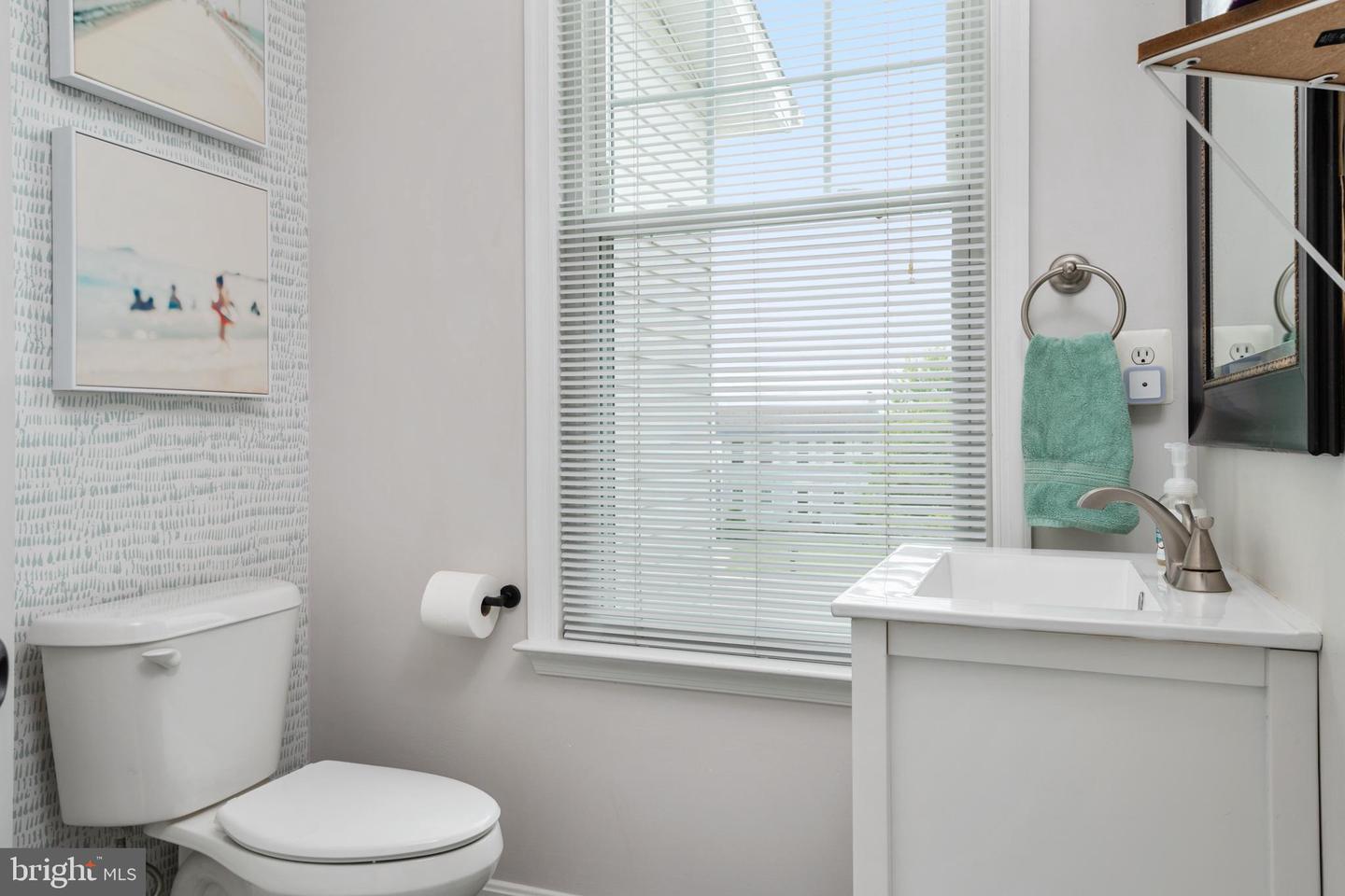 Bathroom with white vanity and toilet, a large window with blinds, and a patterned accent wall.