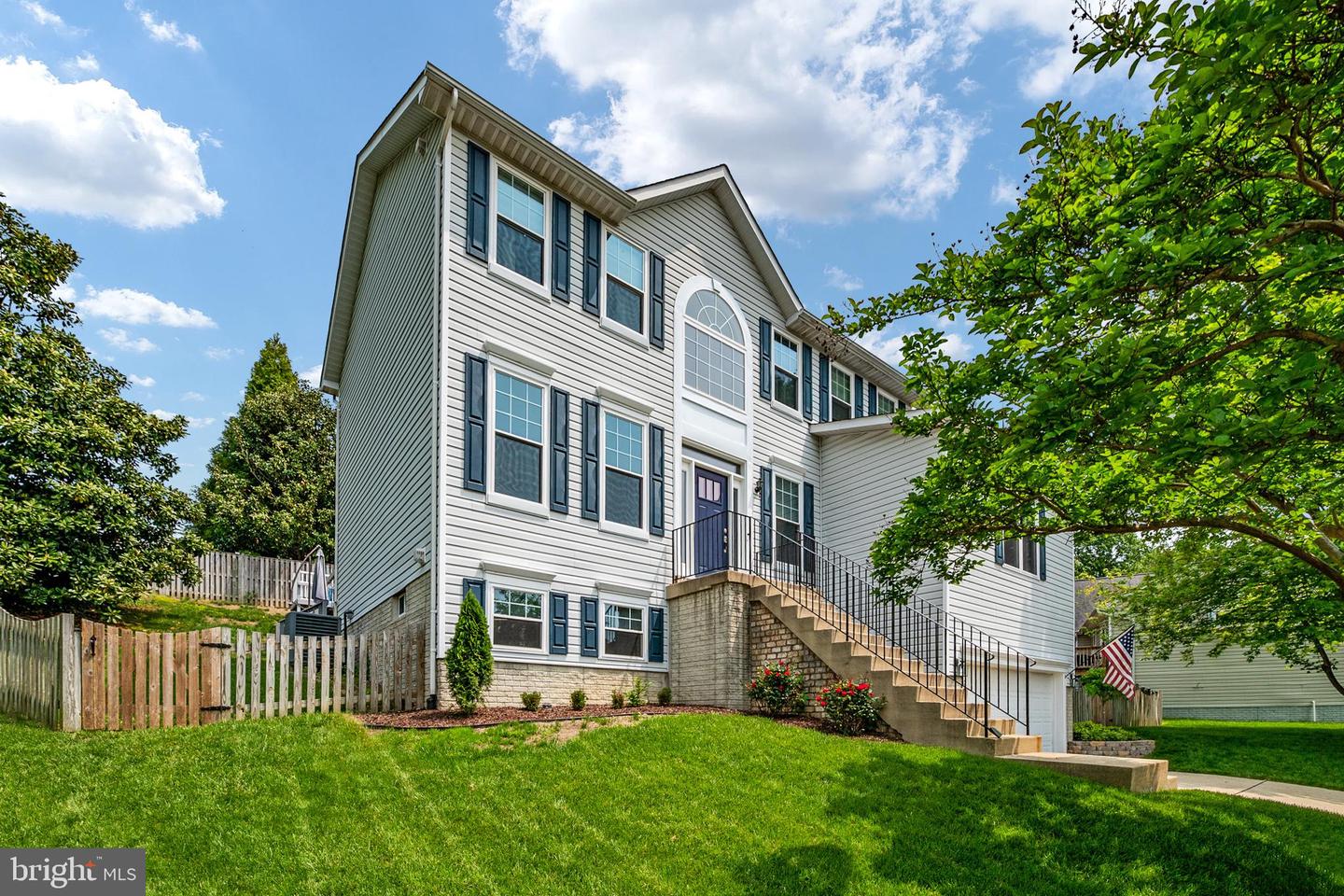 Two-story light-sided house with dark shutters, raised entry steps, and a broad green lawn.
