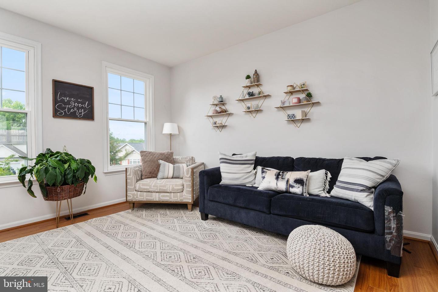 Staged living room with a navy sofa, geometric rug, knitted ottoman, and tall windows.