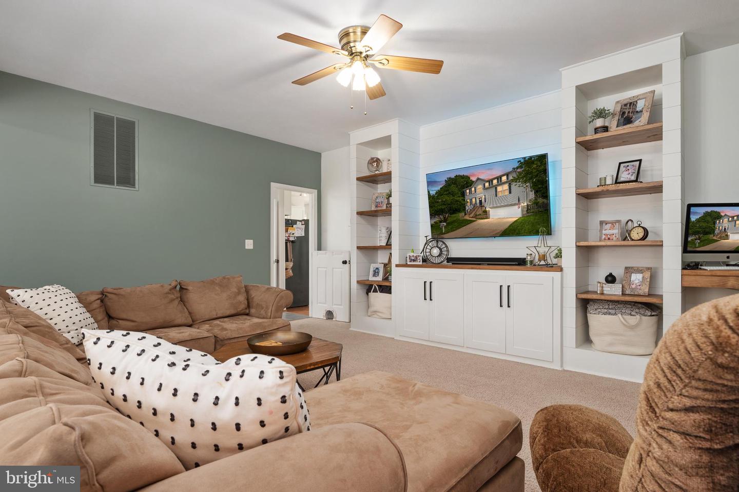 Furnished living room with a beige sectional, built-in shelving, and a white shiplap media wall.