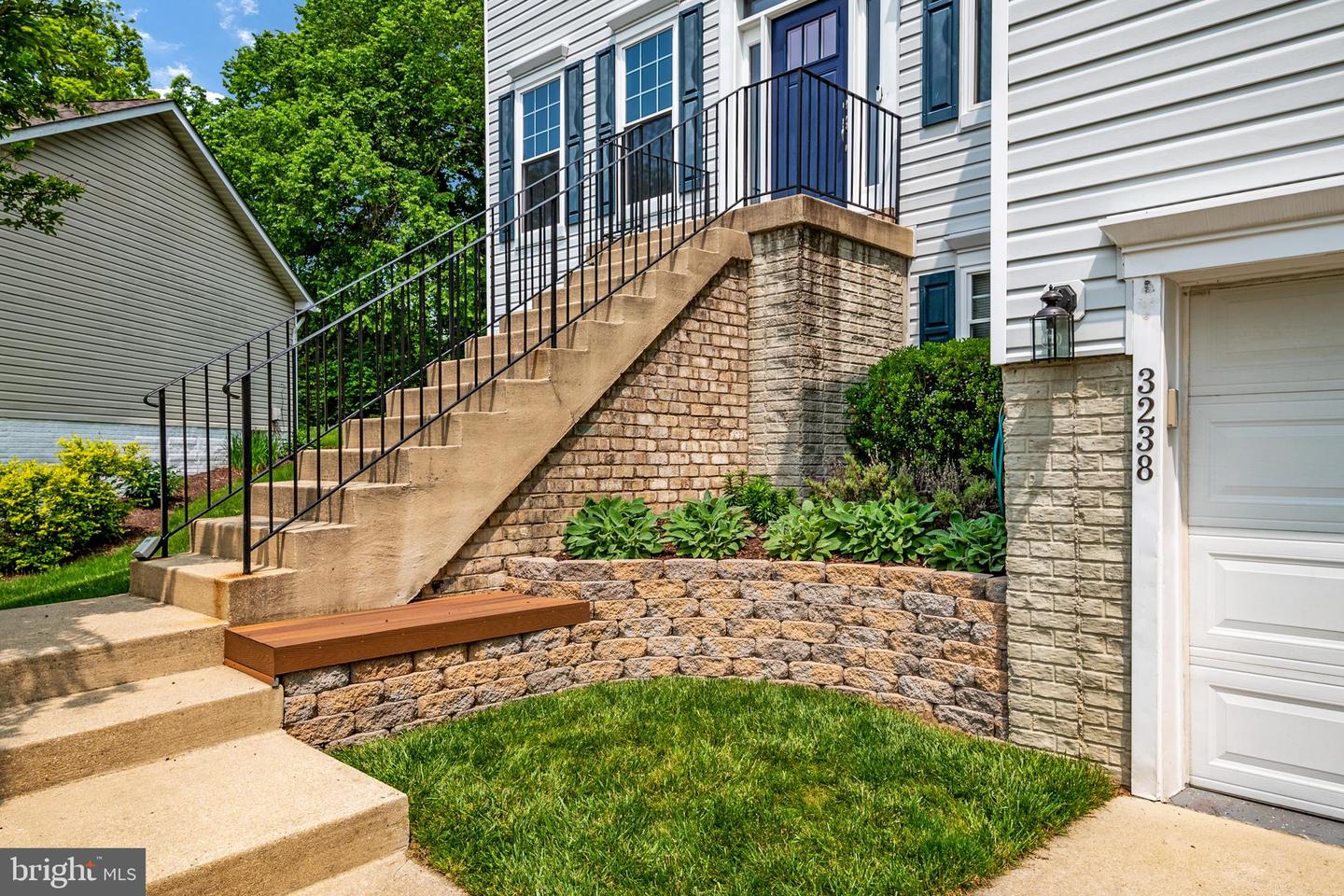 Home entrance with elevated concrete stairs, black railings, stone retaining walls, and landscaped beds.