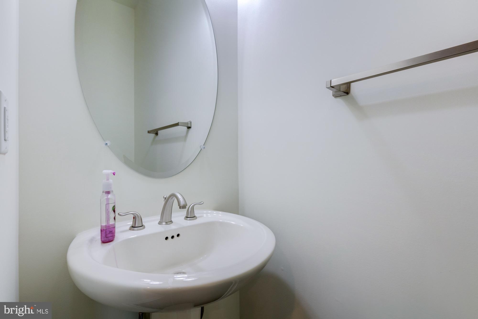 Bathroom sink with brushed-nickel fixtures, oval mirror, and wall-mounted towel bar.