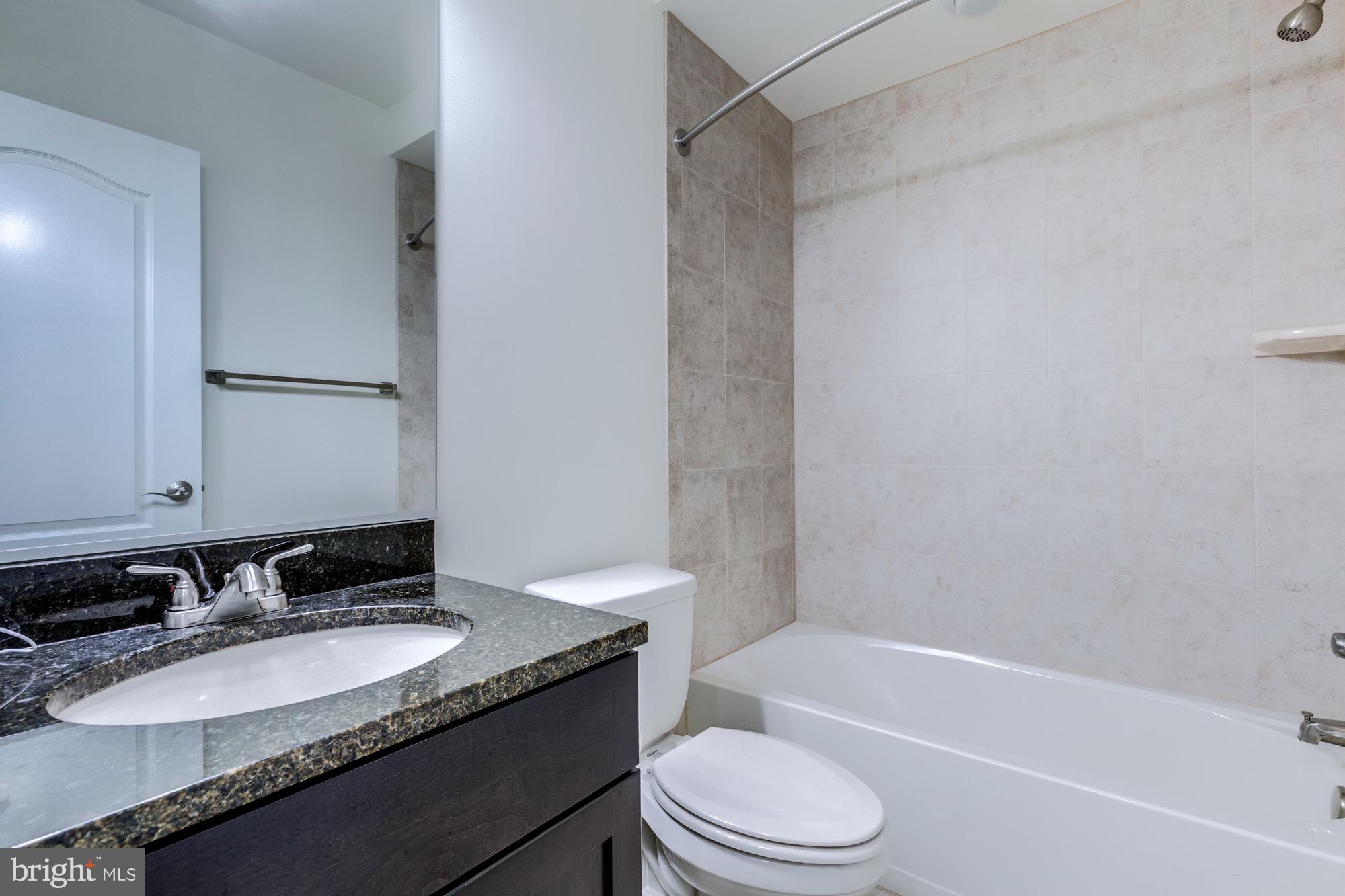 Bathroom with a dark stone vanity, white sink, toilet, and beige-tiled bathtub surround.