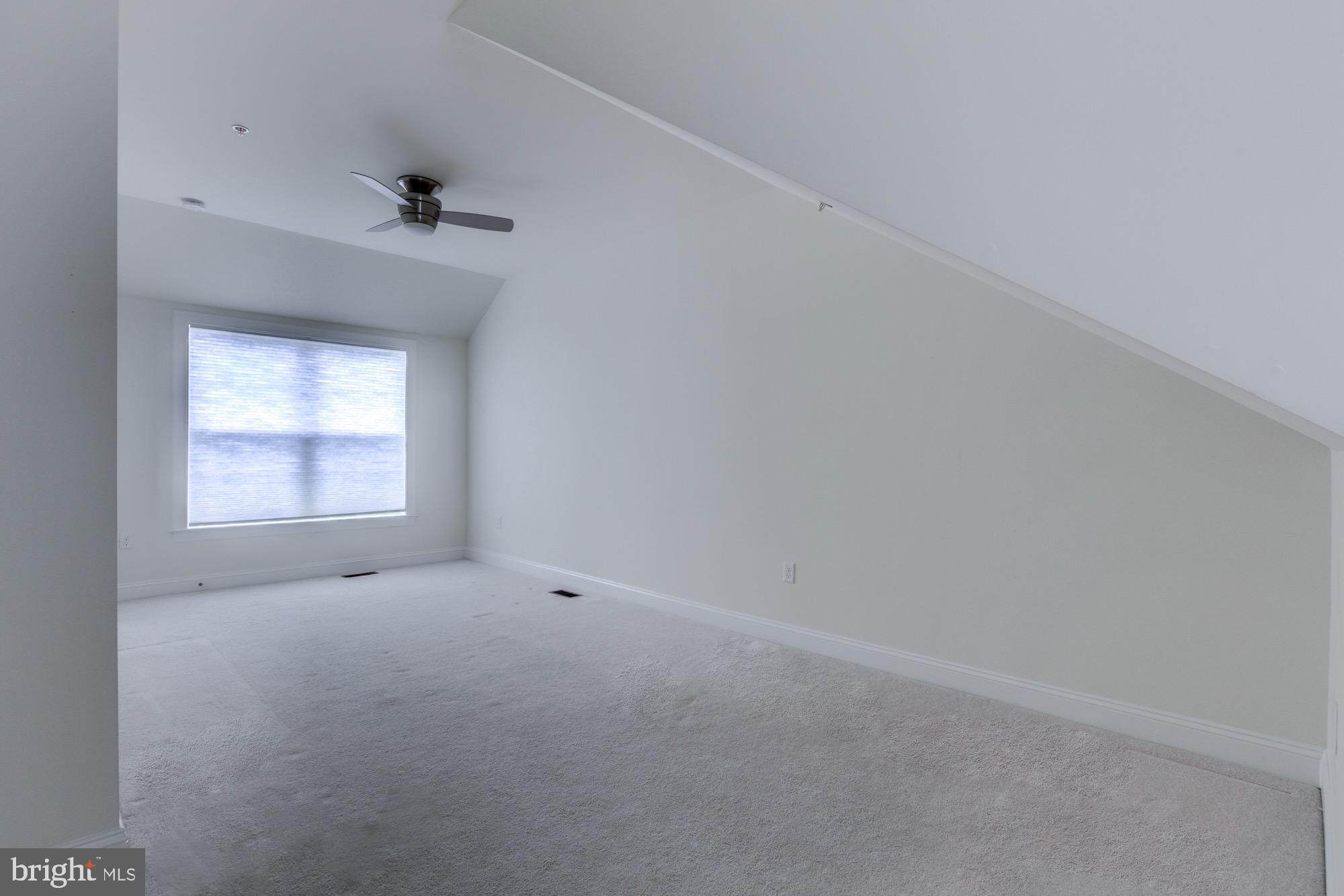 Empty carpeted room with a sloped ceiling, ceiling fan, and shaded window.