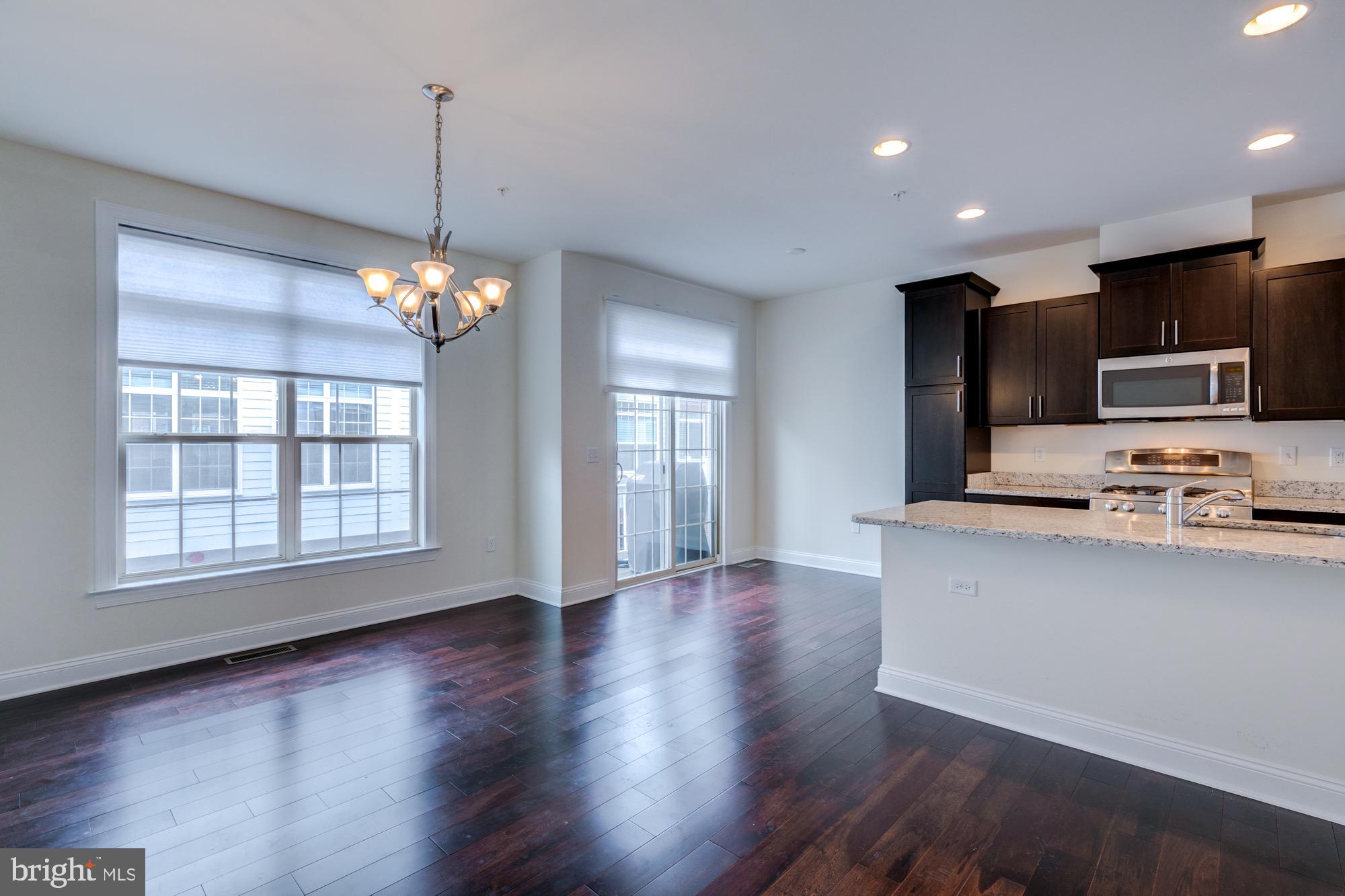 Open kitchen and dining area with dark hardwood floors, dark cabinets, and a granite breakfast bar.