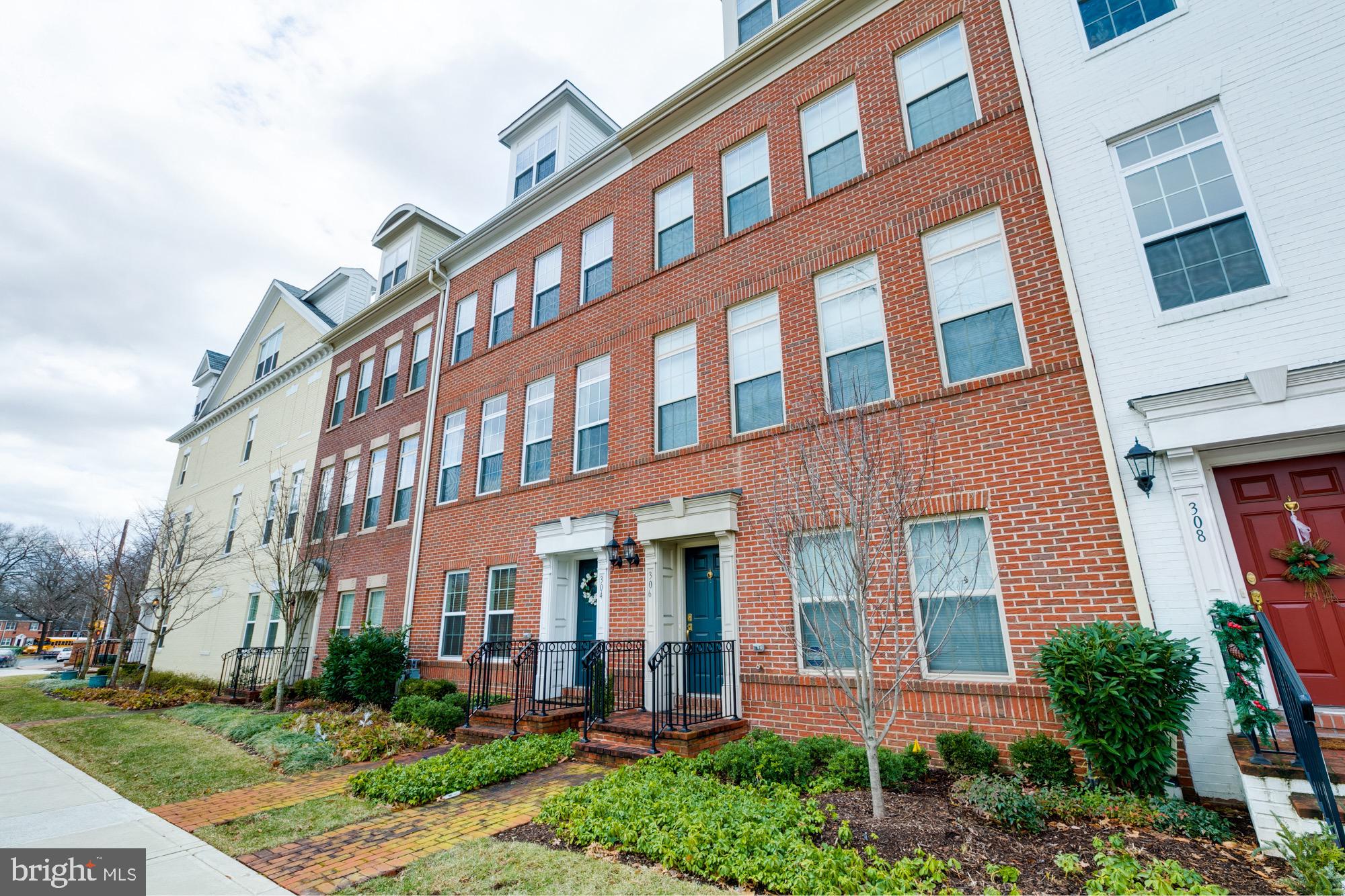 Red-brick townhouse with blue front door, brick stoop, black railings, and landscaped front garden.