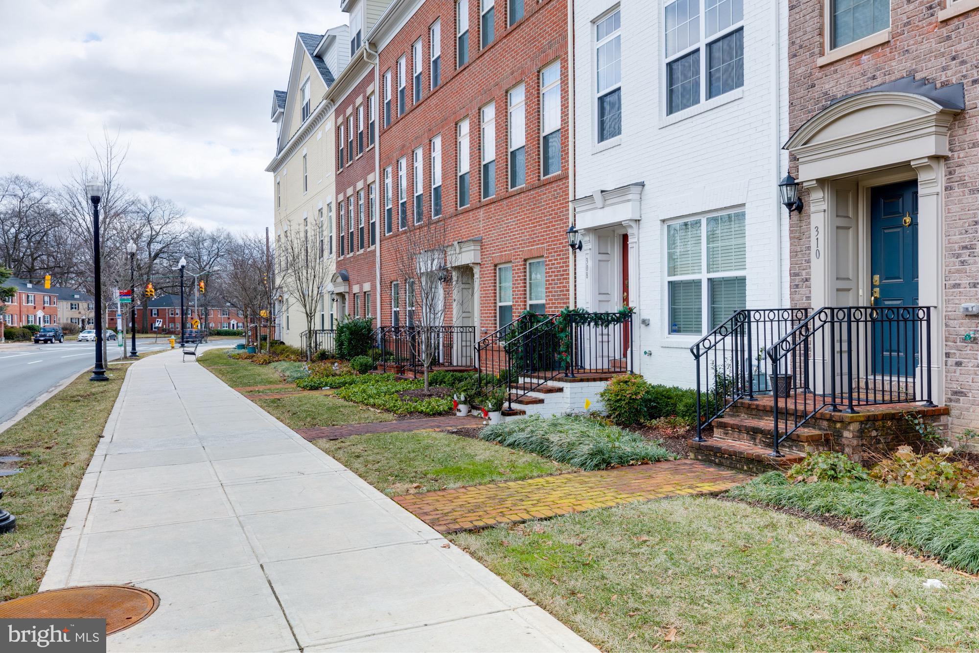 Row of brick townhouses with stoops and black railings along a sidewalk.