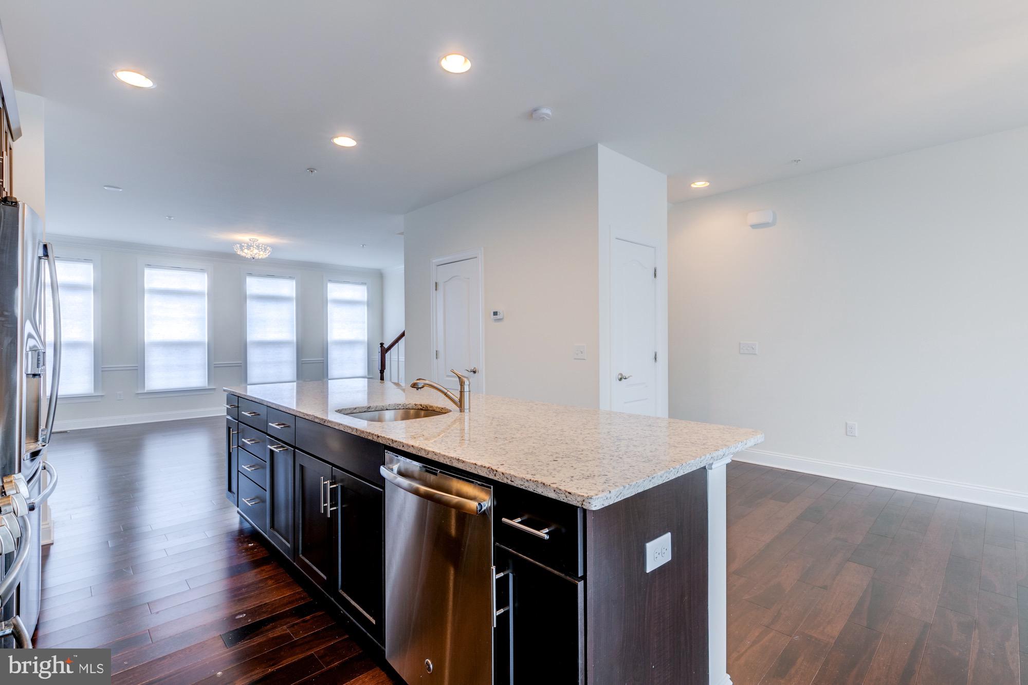 Kitchen with a large granite island, dark cabinets, stainless steel appliances, and tall shaded windows.