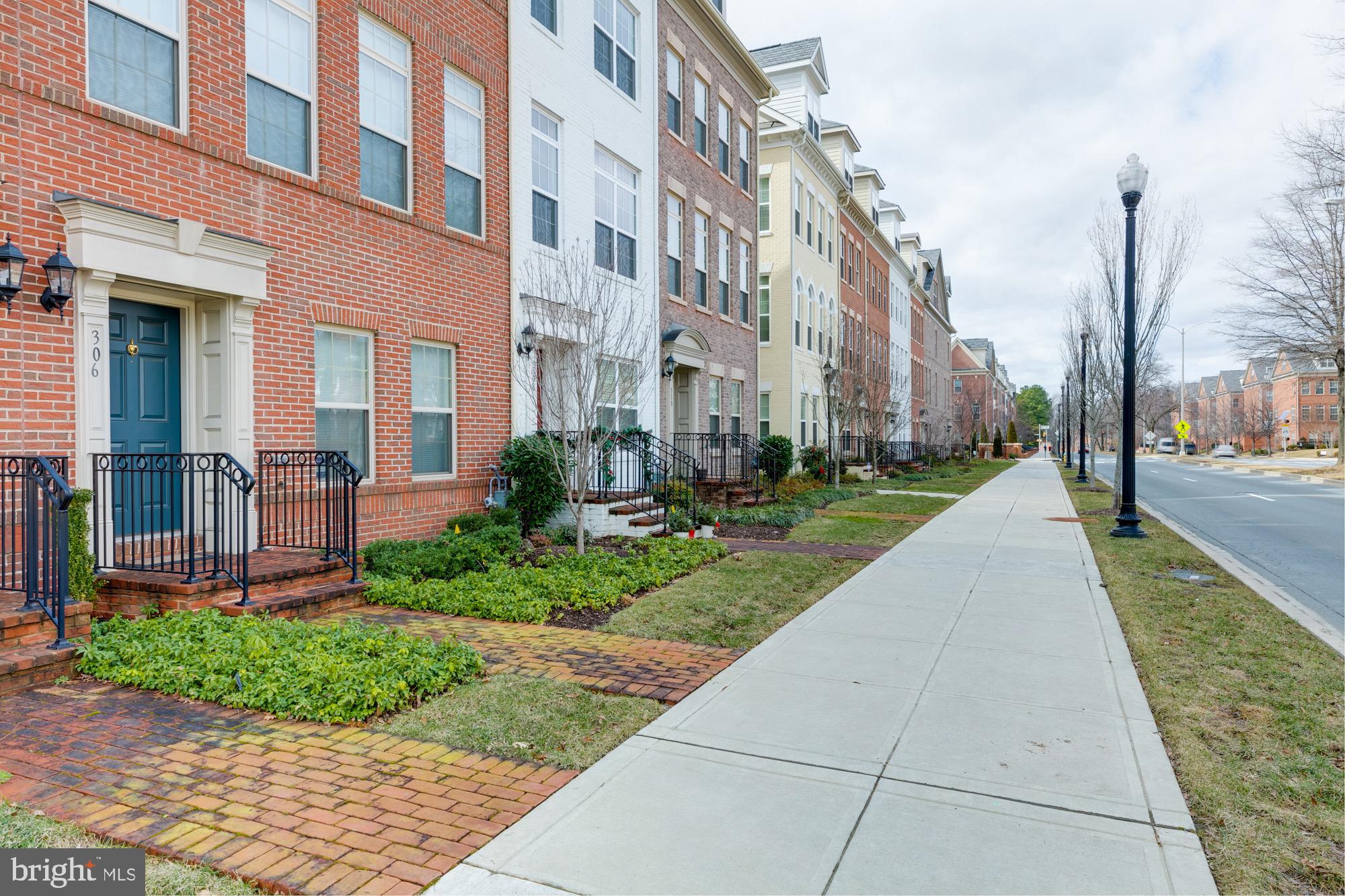 Red-brick townhome with a blue front door and brick stoop along a tree-lined sidewalk.