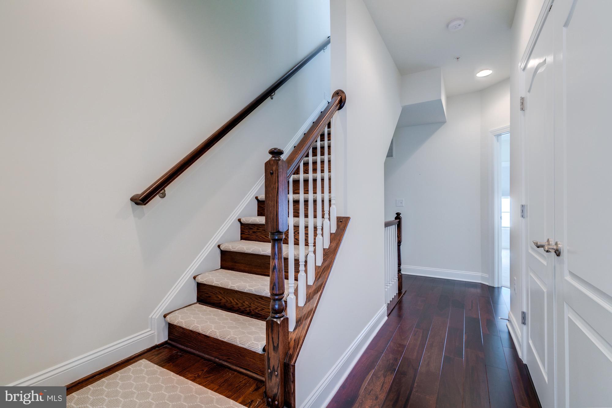 Staircase with carpeted treads and dark wood railing beside a hardwood hallway.