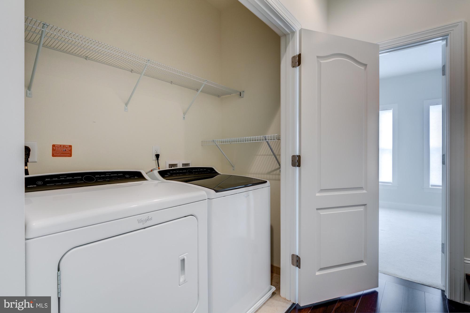 Laundry room with white washer and dryer, wire shelving, and an open door to a bright room.