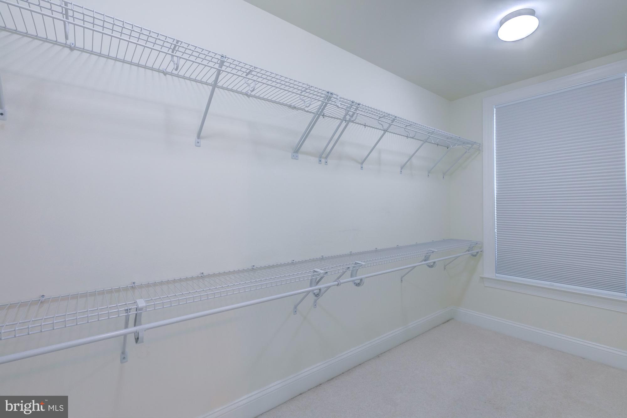Walk-in closet with extensive wire shelving, hanging rods, and a window with a closed blind.