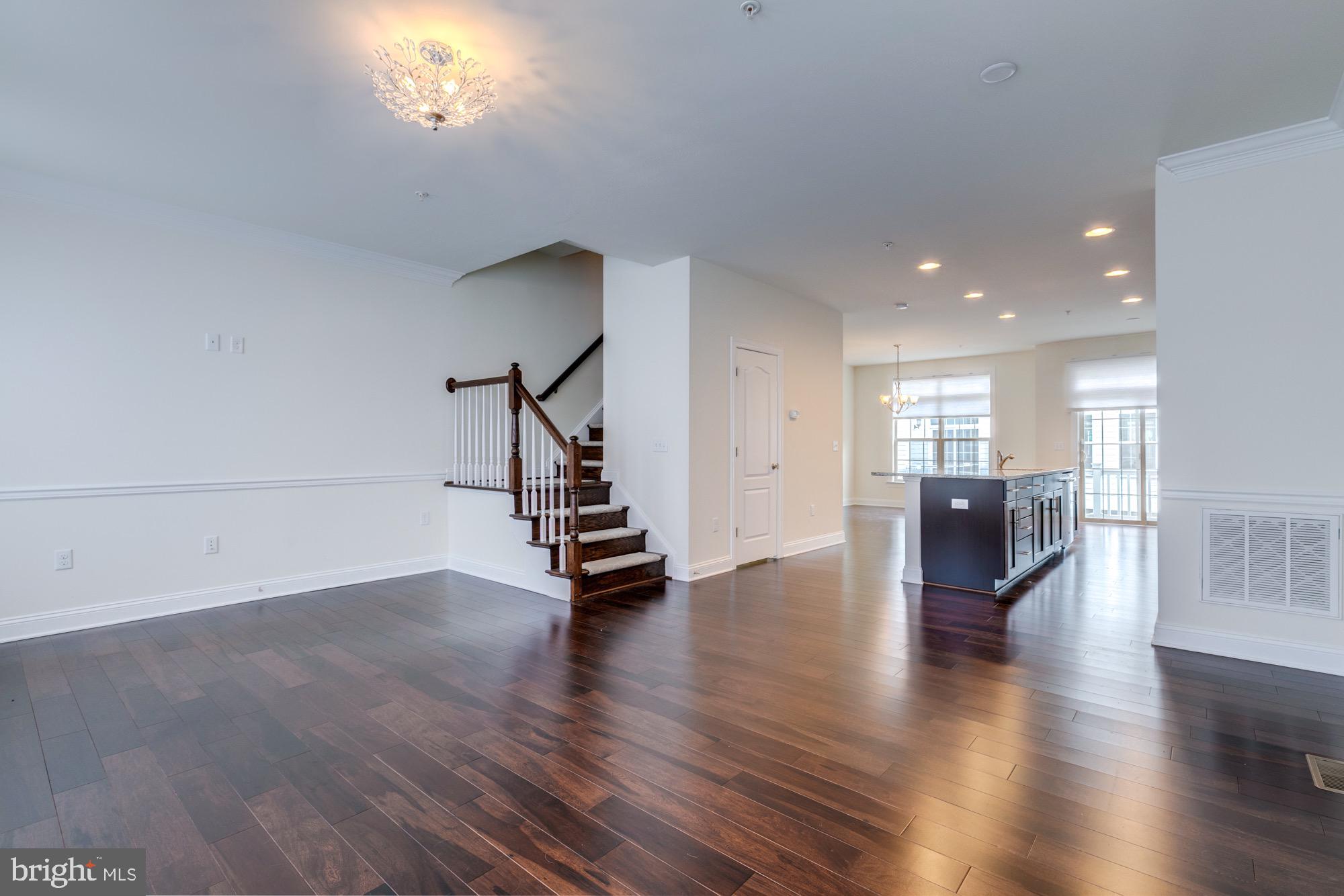 Open kitchen and living area with a dark island, hardwood floors, and staircase.