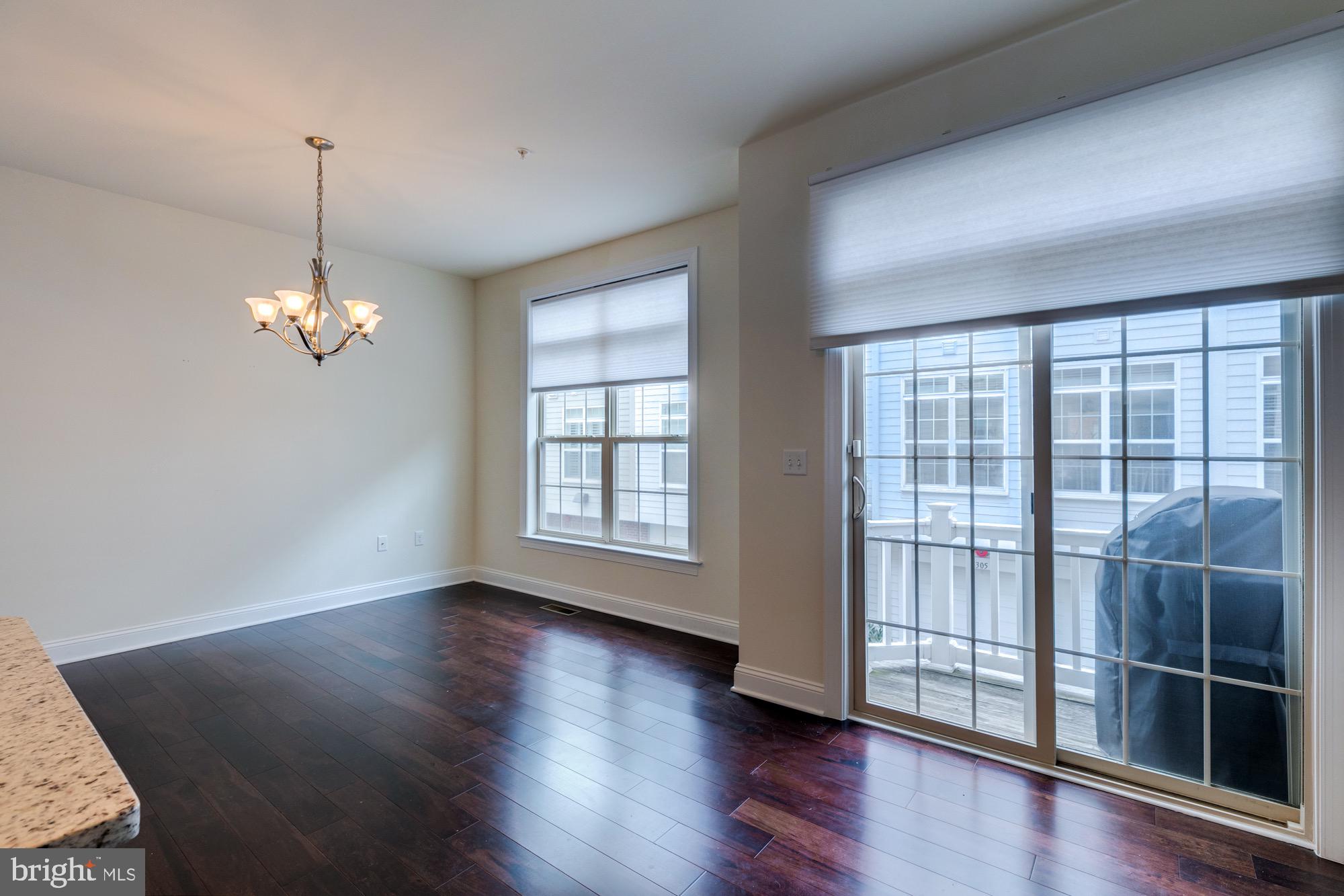 Unfurnished dining area with dark hardwood floors, a chandelier, and sliding glass doors to a balcony.