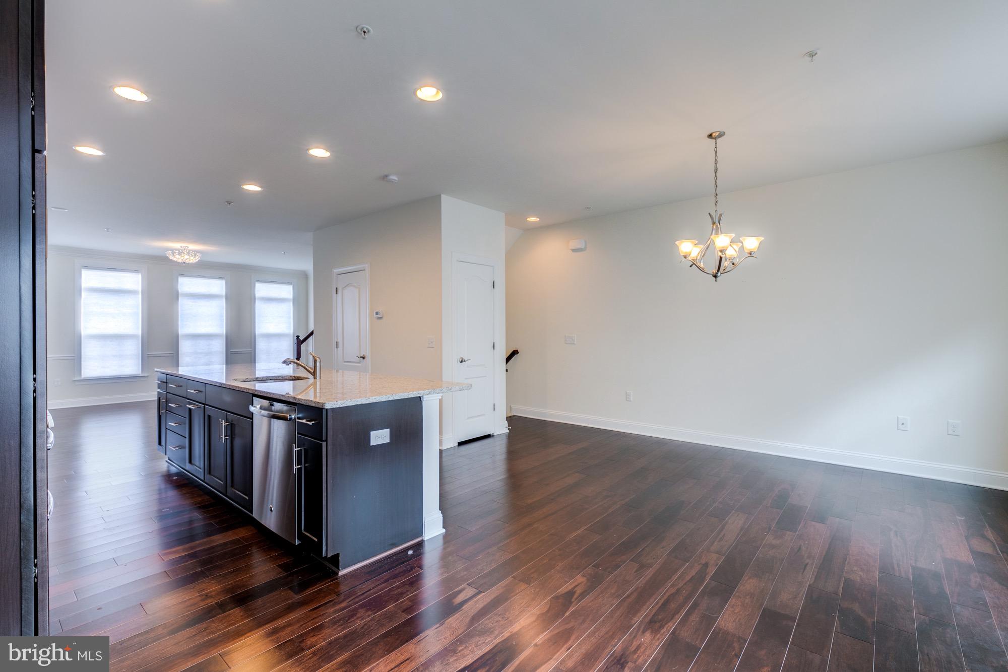 Open kitchen and dining area with a dark island, hardwood floors, and a dining chandelier.