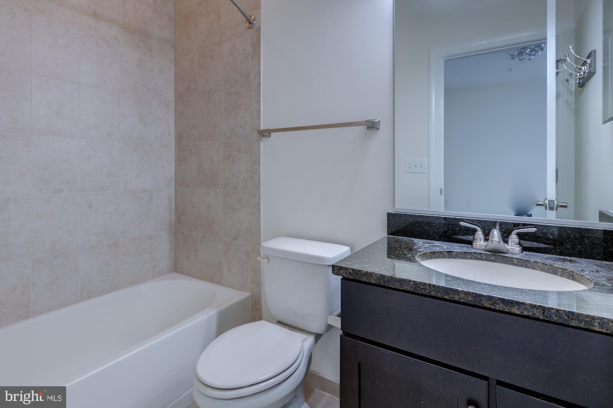 Bathroom with a tiled bathtub, toilet, and dark granite vanity.