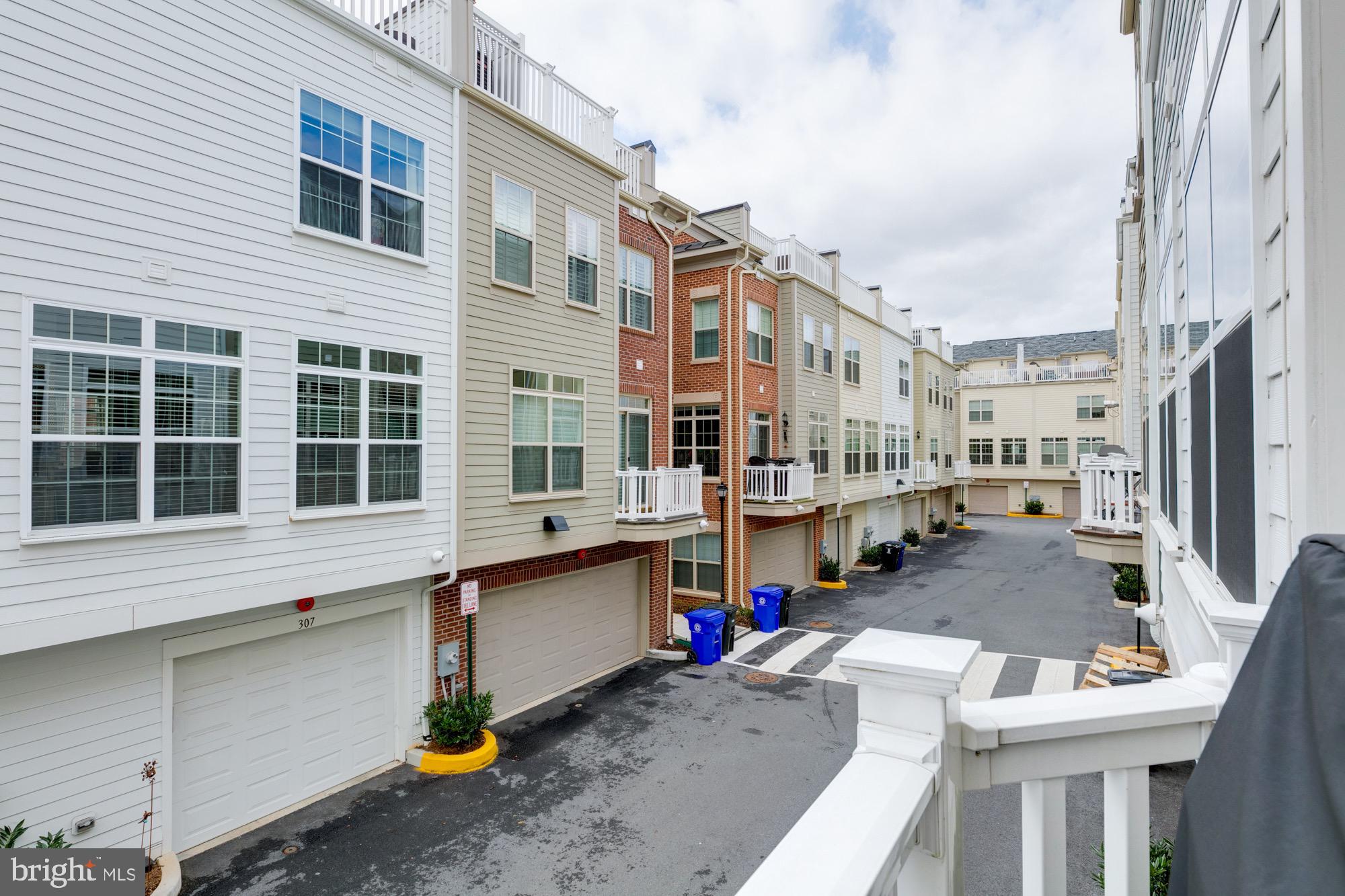 Townhome alley lined with attached homes, garage doors, balconies, and white railings.