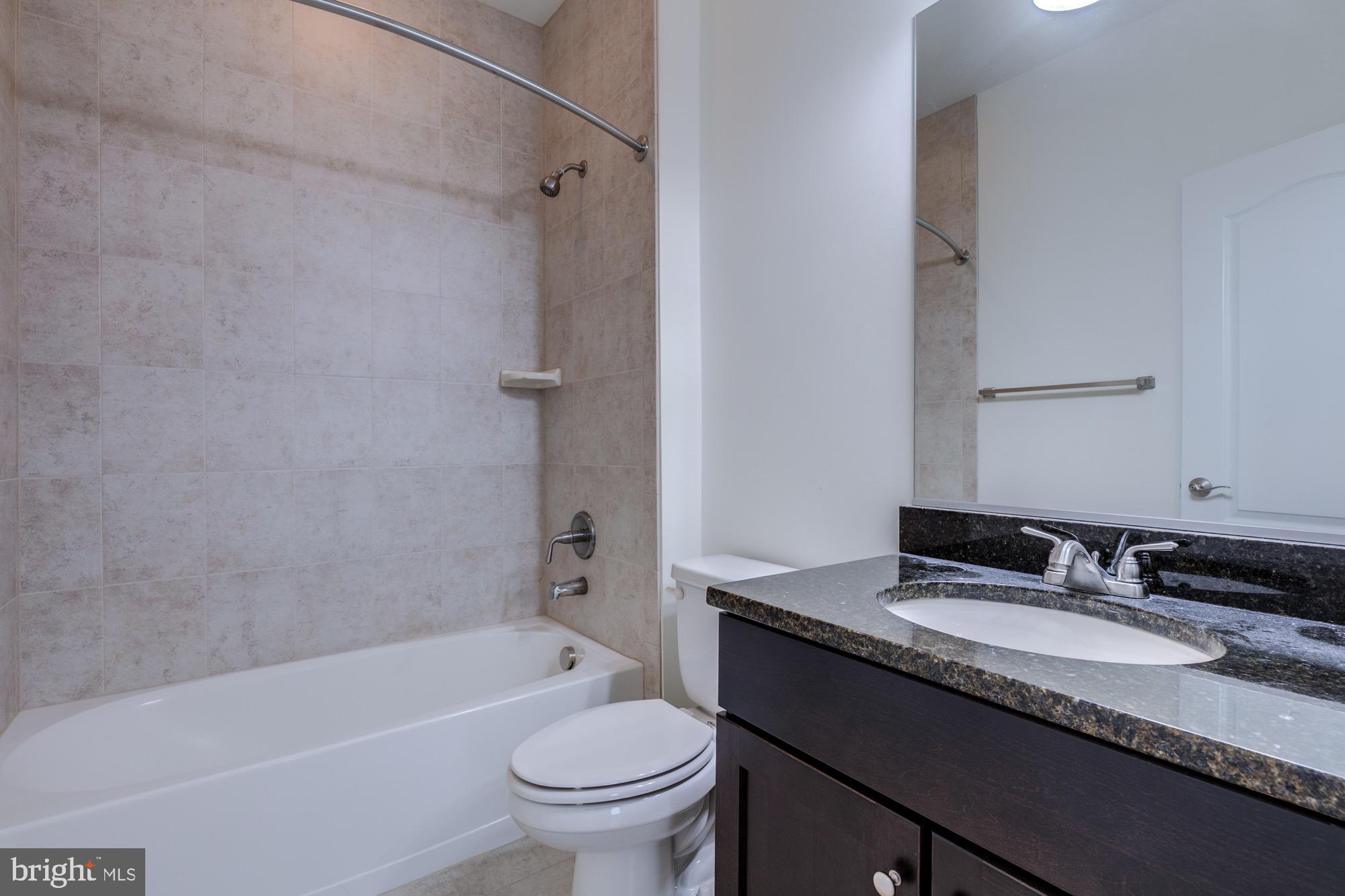 Bathroom with a beige-tiled tub and dark vanity with a stone countertop.