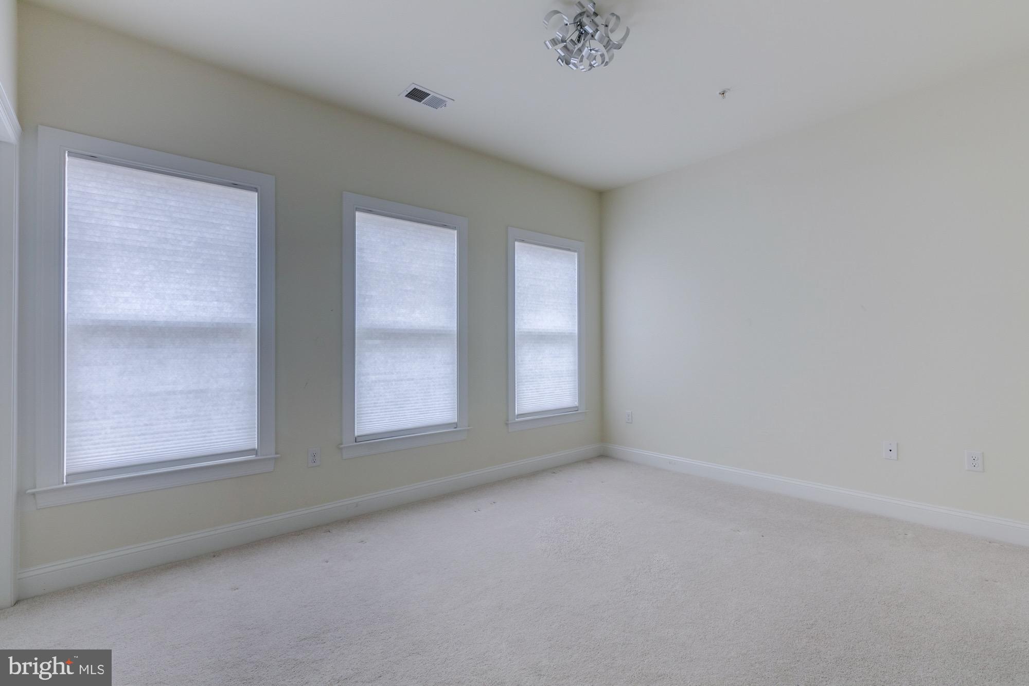 Vacant carpeted room with three shaded windows and a modern ceiling light.