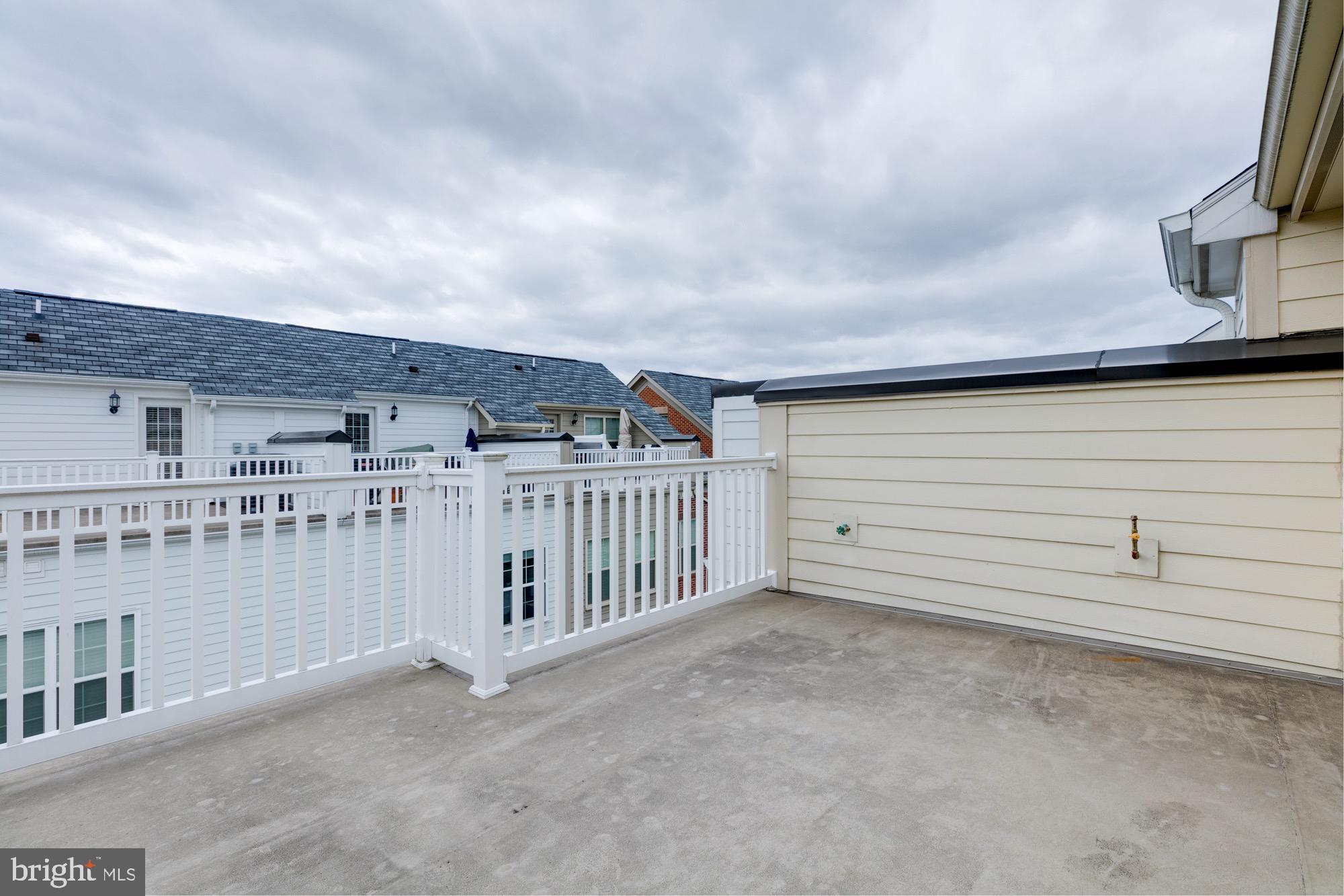 Rooftop terrace with concrete flooring, white railings, and views of neighboring homes.