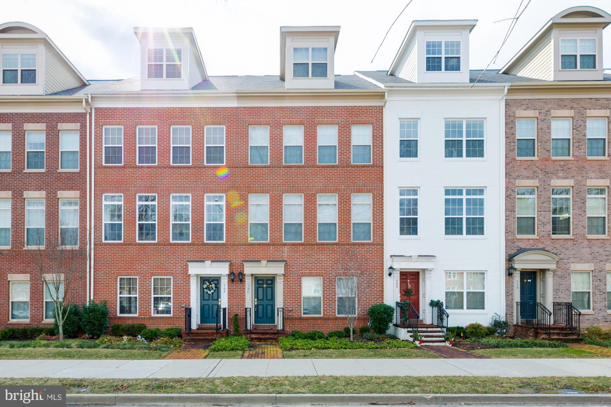 Brick and white townhouse row with dormer windows, landscaped gardens, and front entry walkways.