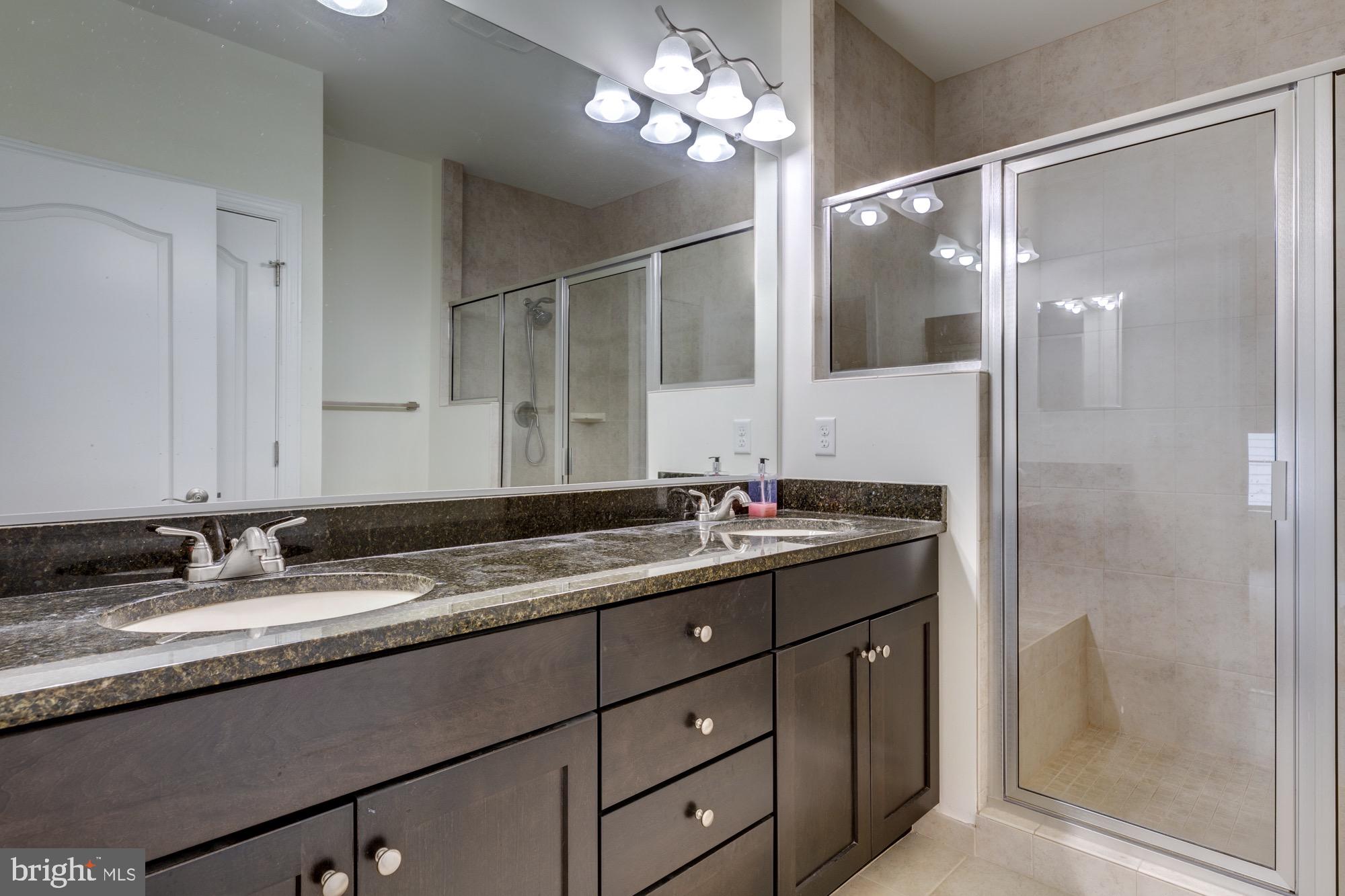 Bathroom with a granite double vanity and glass-enclosed tiled shower.