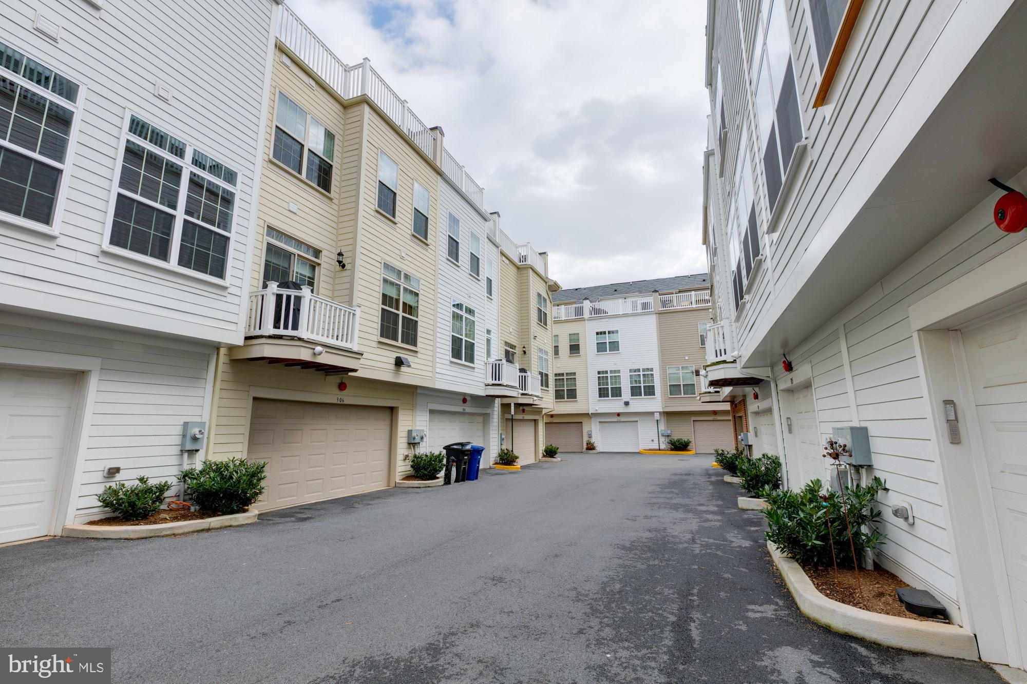 Attached townhouses with garage doors and balconies along a paved shared driveway.