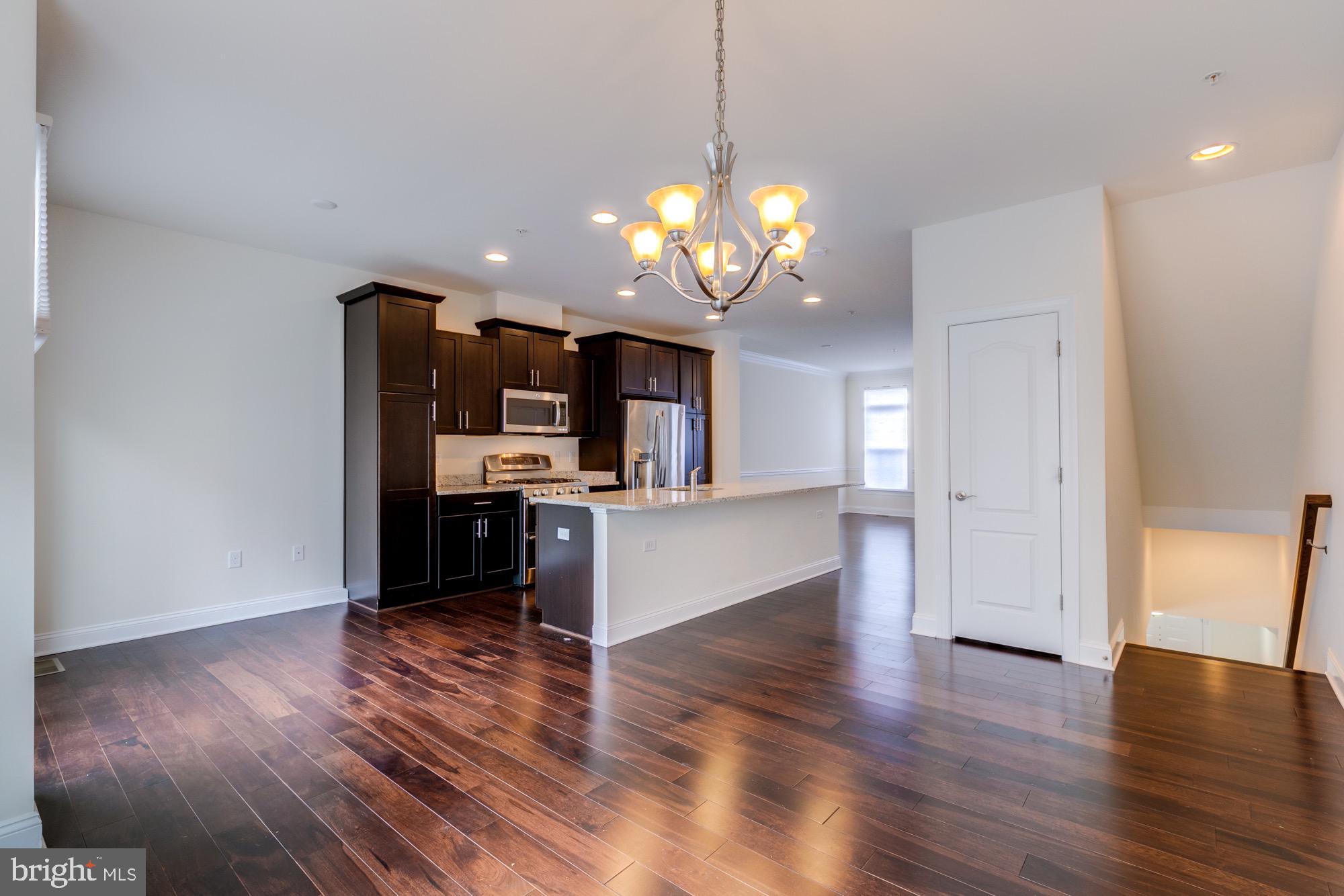 Open kitchen with dark wood cabinets, stainless steel appliances, granite island, and dark hardwood floors.