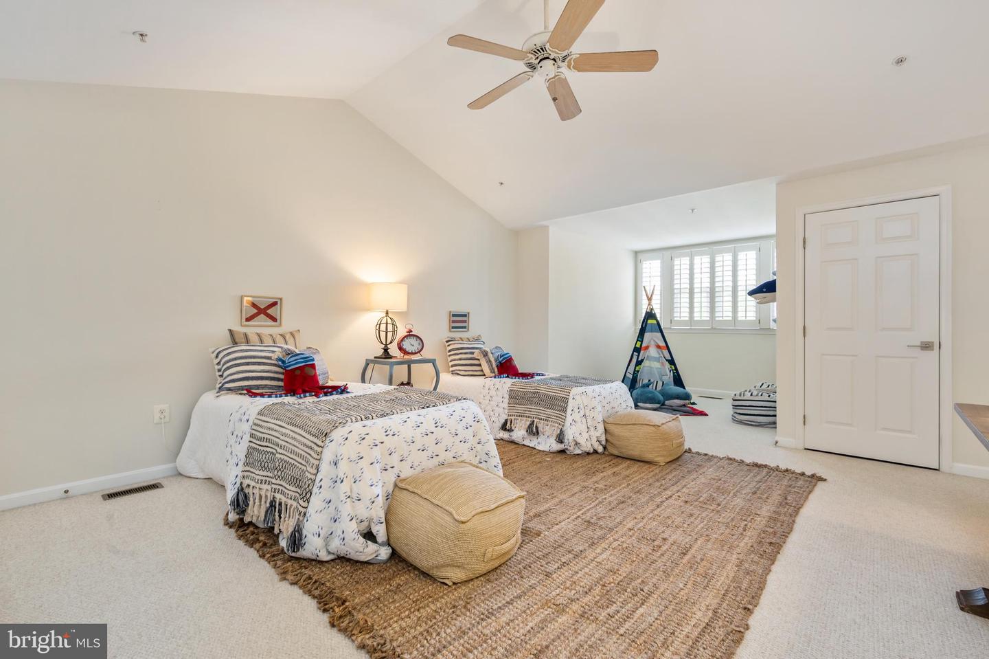 Staged bedroom with two beds, a sloped ceiling, ceiling fan, and plantation-shuttered window.