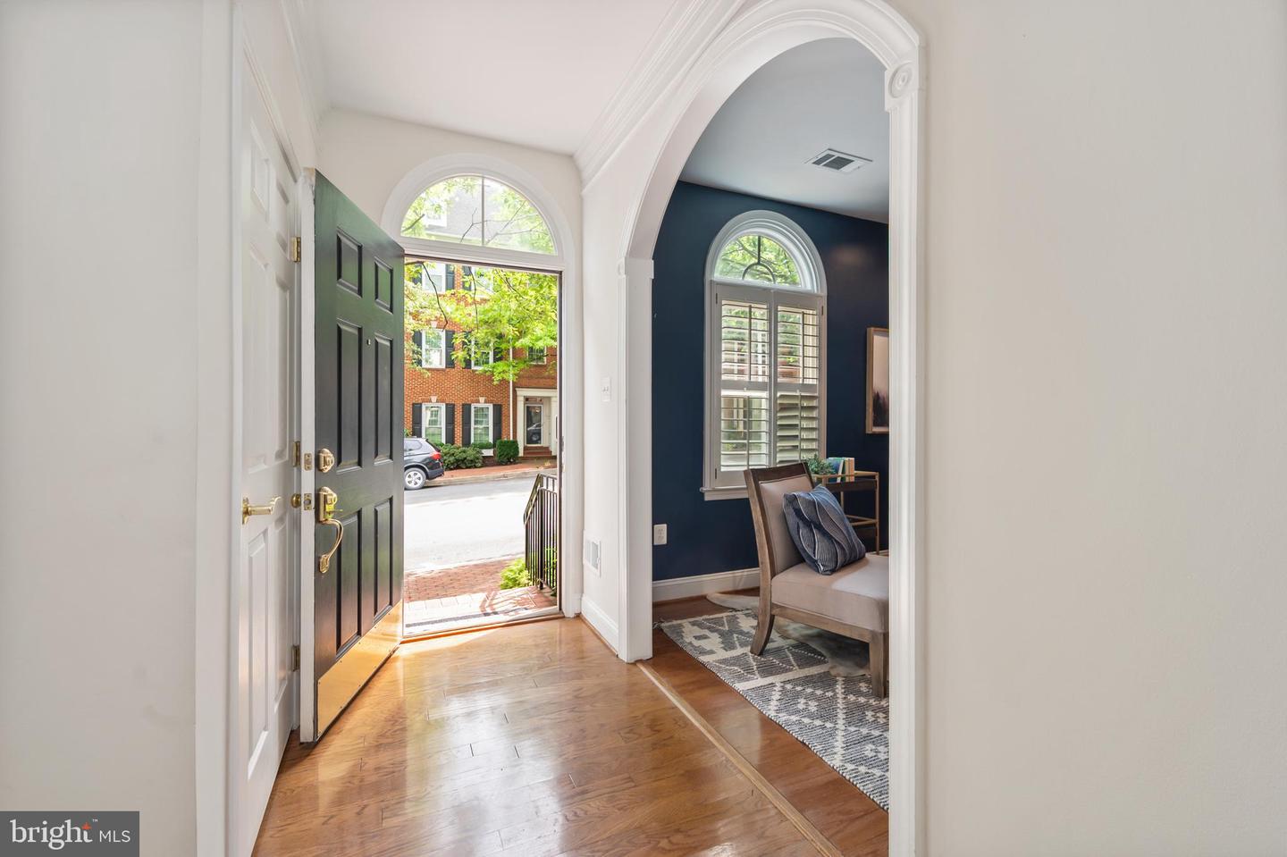 Furnished entryway with hardwood floors, open front door, and an arched opening to a navy sitting room.