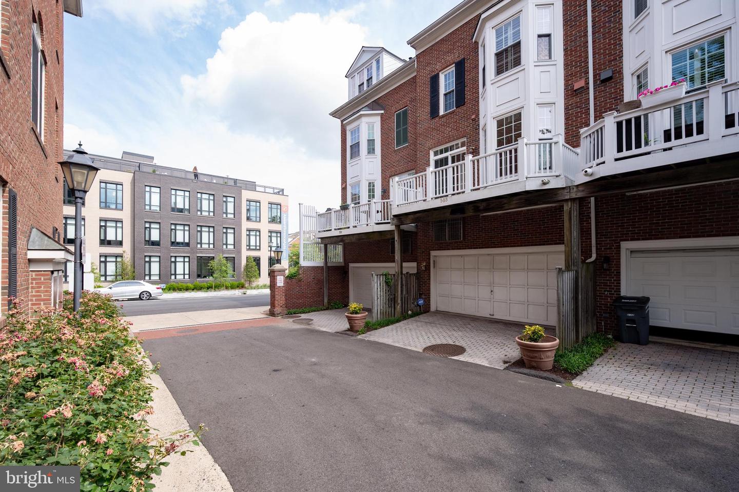 Brick townhome exterior with white elevated deck, garage doors, and paved alley.