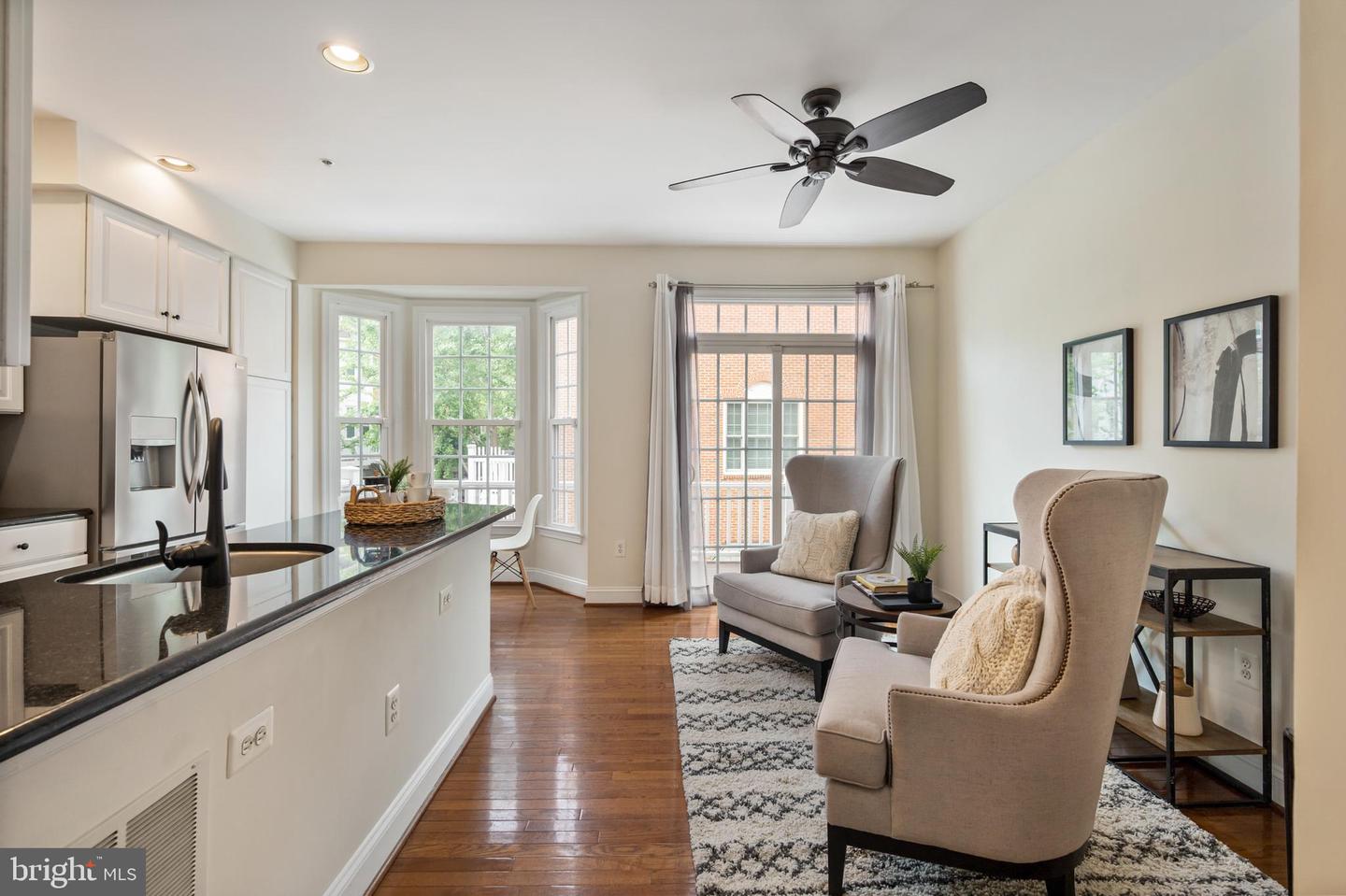 Open kitchen and living area with white cabinetry, hardwood floors, bay windows, and upholstered seating.