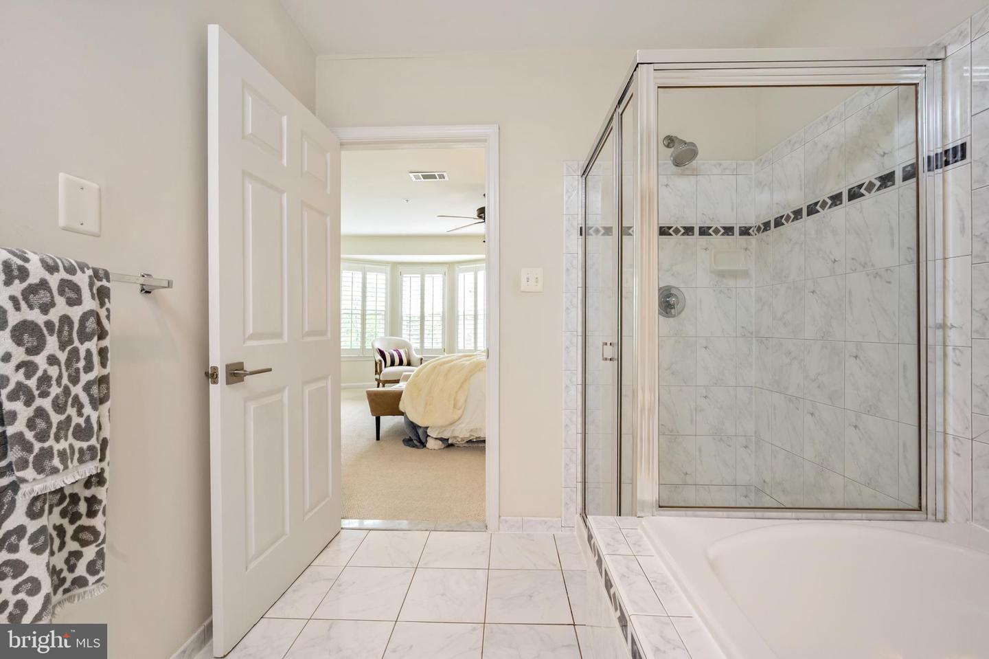 Bathroom with a tiled bathtub and glass-enclosed shower, opening onto a furnished bedroom.